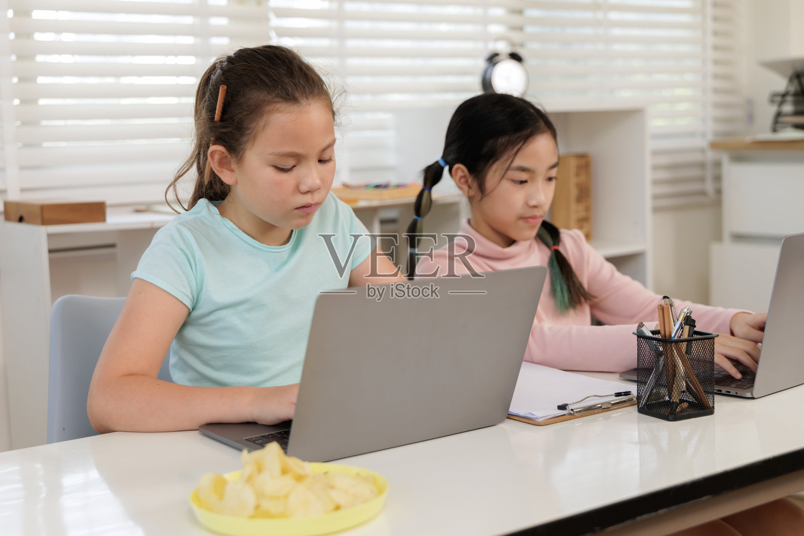 两个女孩专注于在线课堂,可能是在教室或家中。照片摄影图片
