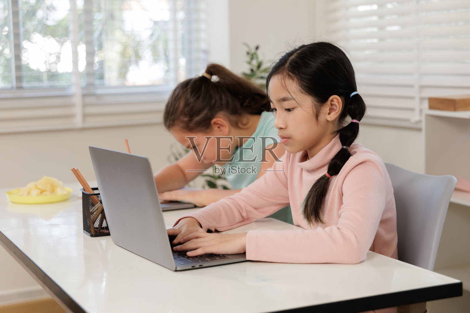 两个女孩专注地参加在线课程,可能是在教室或家中。照片摄影图片