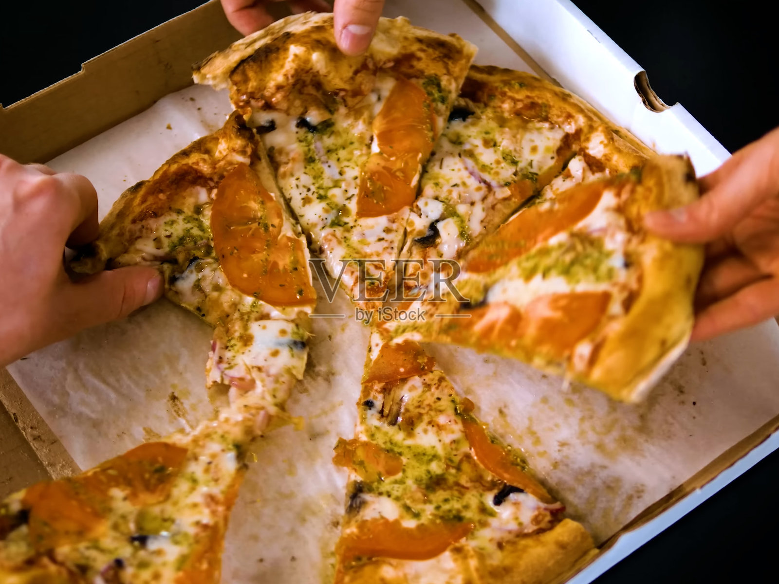 几个人从刚送达的盒子里分取热腾腾的火腿披萨,特写镜头美丽。照片摄影图片