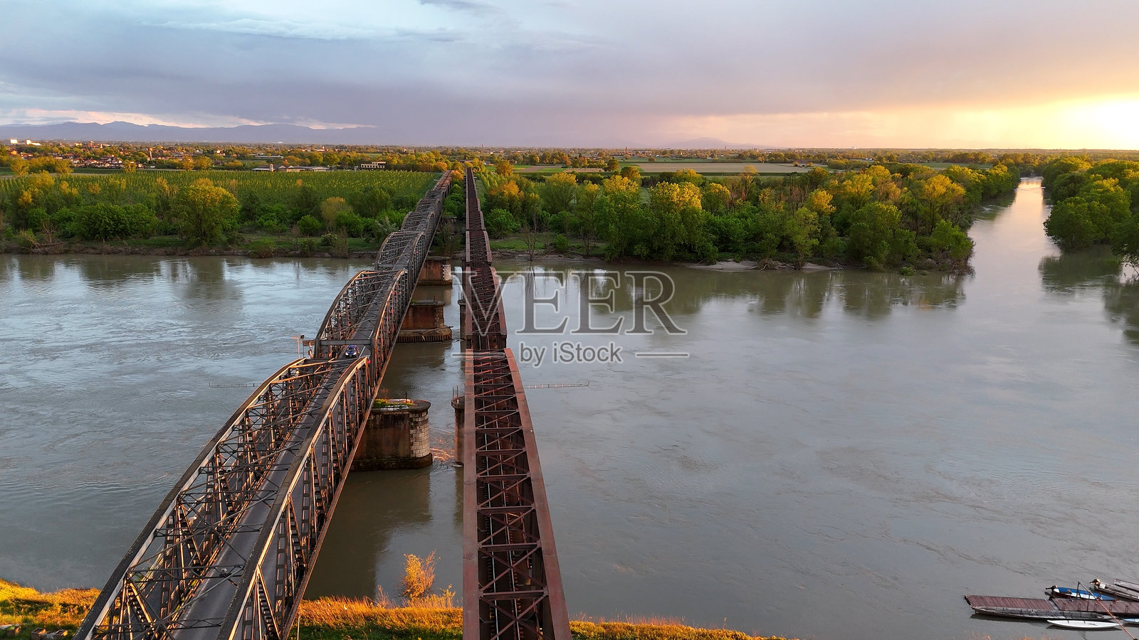意大利克雷莫纳附近跨越波河的金属高架桥,金色日落照亮了建筑结构和黄昏时分的美丽河流环境。照片摄影图片
