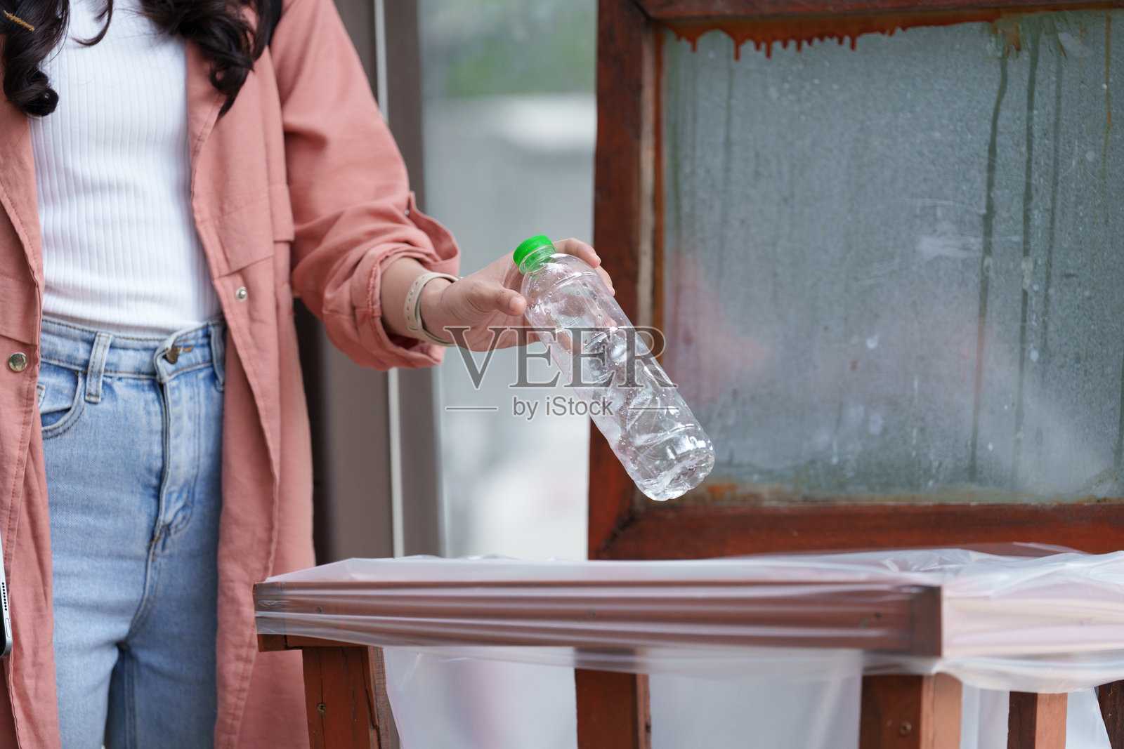 年轻女性将塑料瓶扔进垃圾桶,强调回收的重要性,提高对环境保护和可持续实践的意识照片摄影图片
