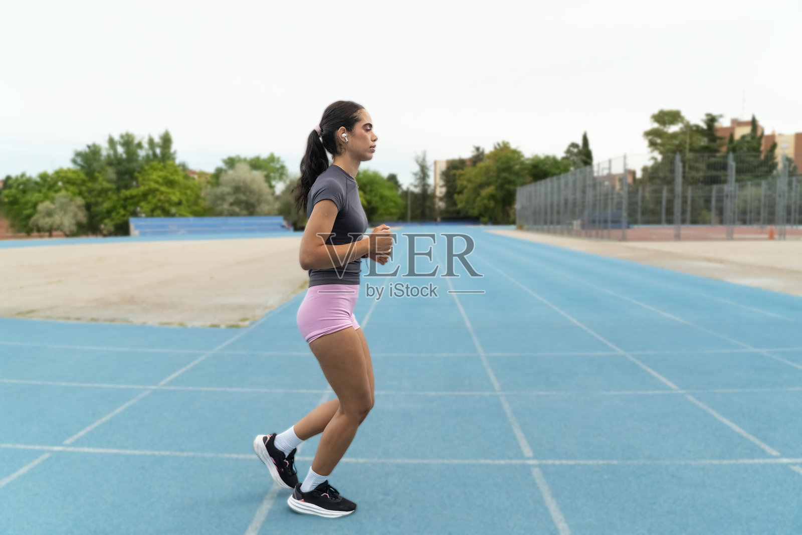 专注的年轻女性在蓝色田径跑道上跑步,佩戴无线耳机听音乐照片摄影图片