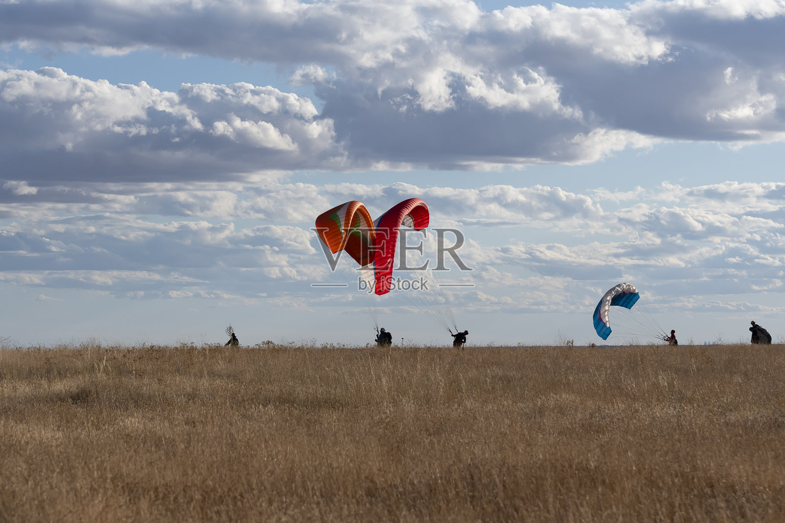 滑翔伞在多云的天空下翱翔于金色田野上,正值下午时分。照片摄影图片