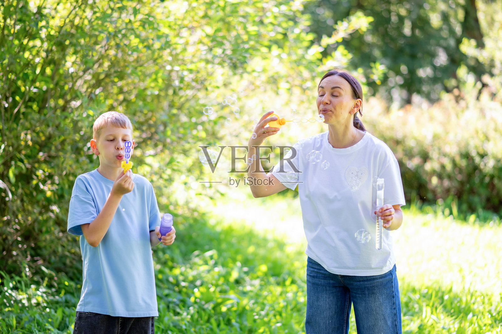 母亲和青少年男孩在夏季公园里快乐地吹泡泡照片摄影图片