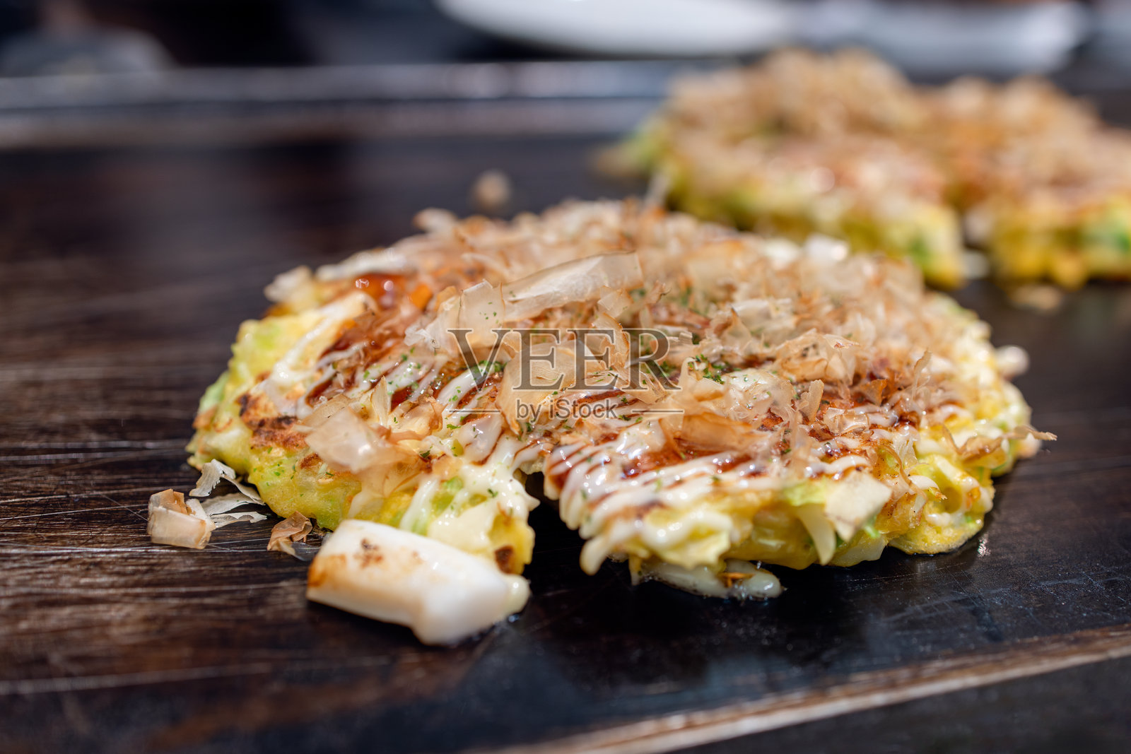 新鲜烤制的御好烧,上面撒有鲣鱼 flakes、酱汁和美乃滋,在日本的热铁板上滋滋作响。照片摄影图片