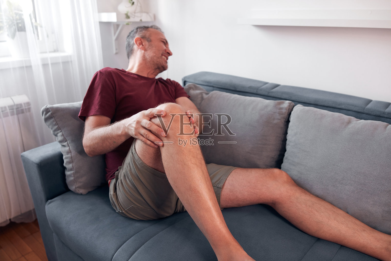 在家中感到膝盖和腿部疼痛的男子。照片摄影图片