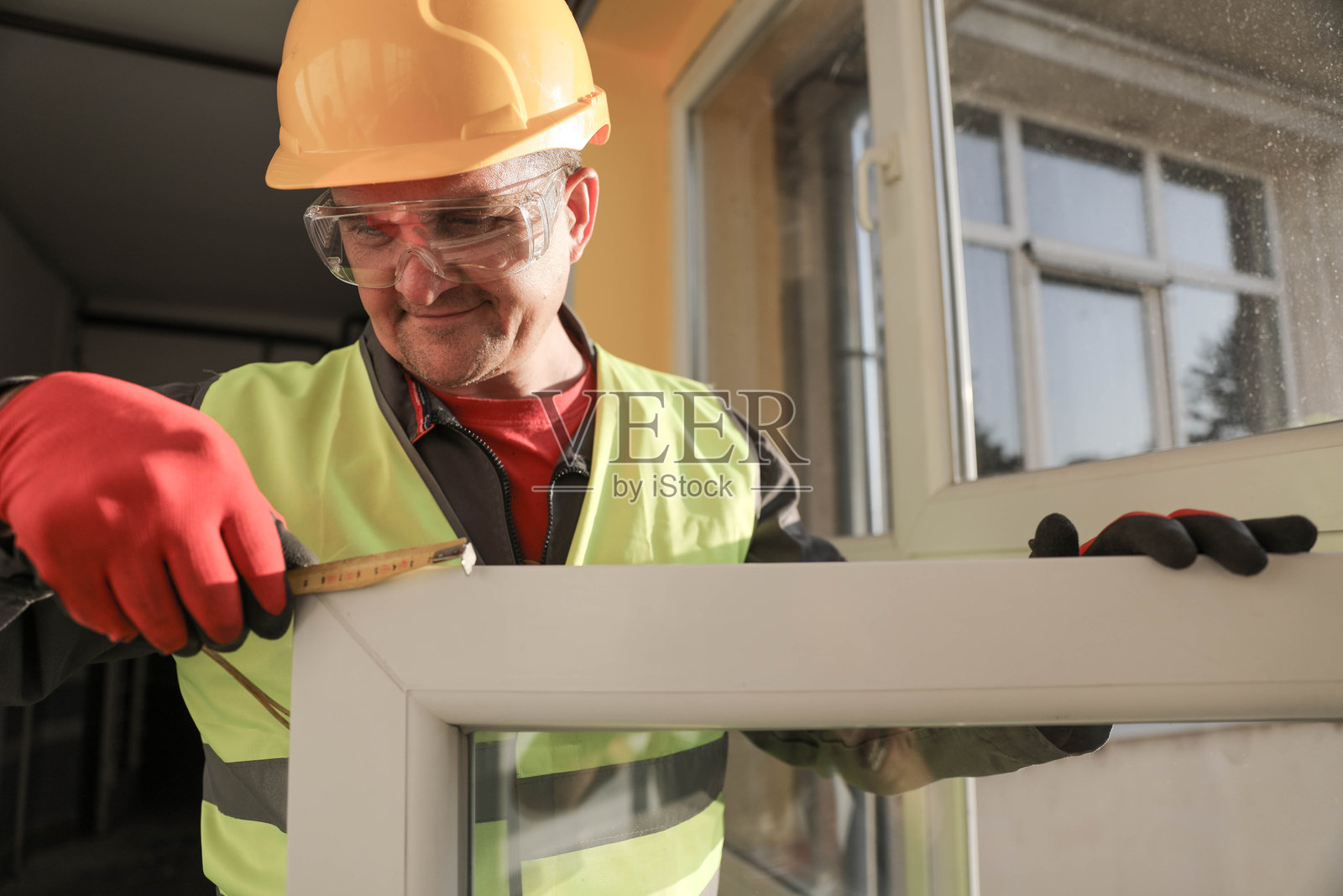 穿着头盔和背心的高级技术员正在测量窗框照片摄影图片