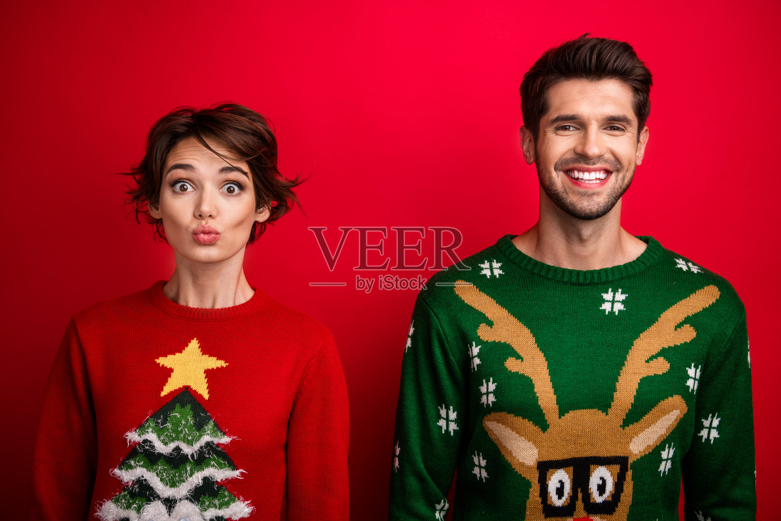 穿着丑陋毛衣的兴奋夫妻,嘴唇撅起,背景为红色。照片摄影图片