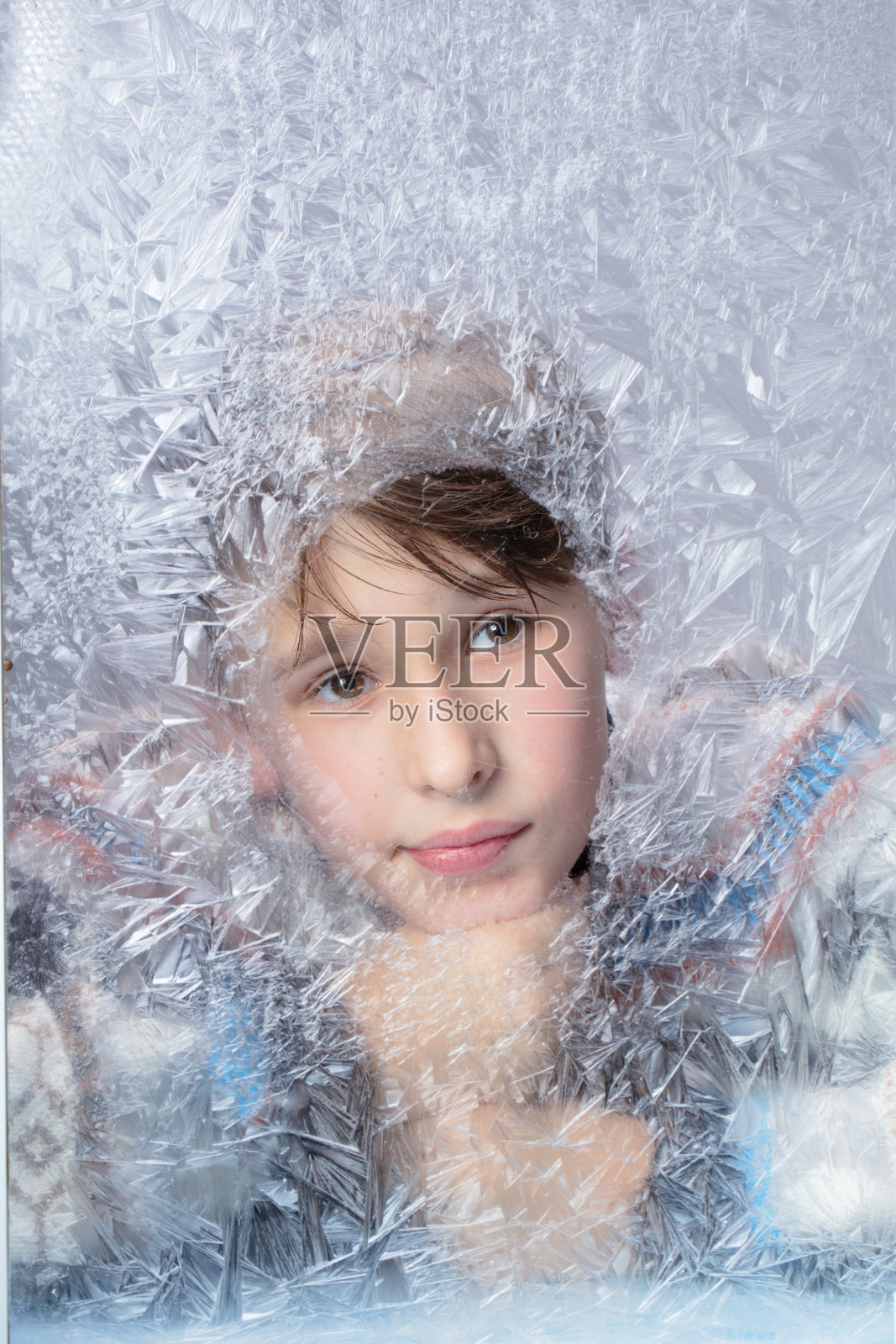 帅气而深思的男孩透过冰冻的玻璃。冬季肖像。照片摄影图片