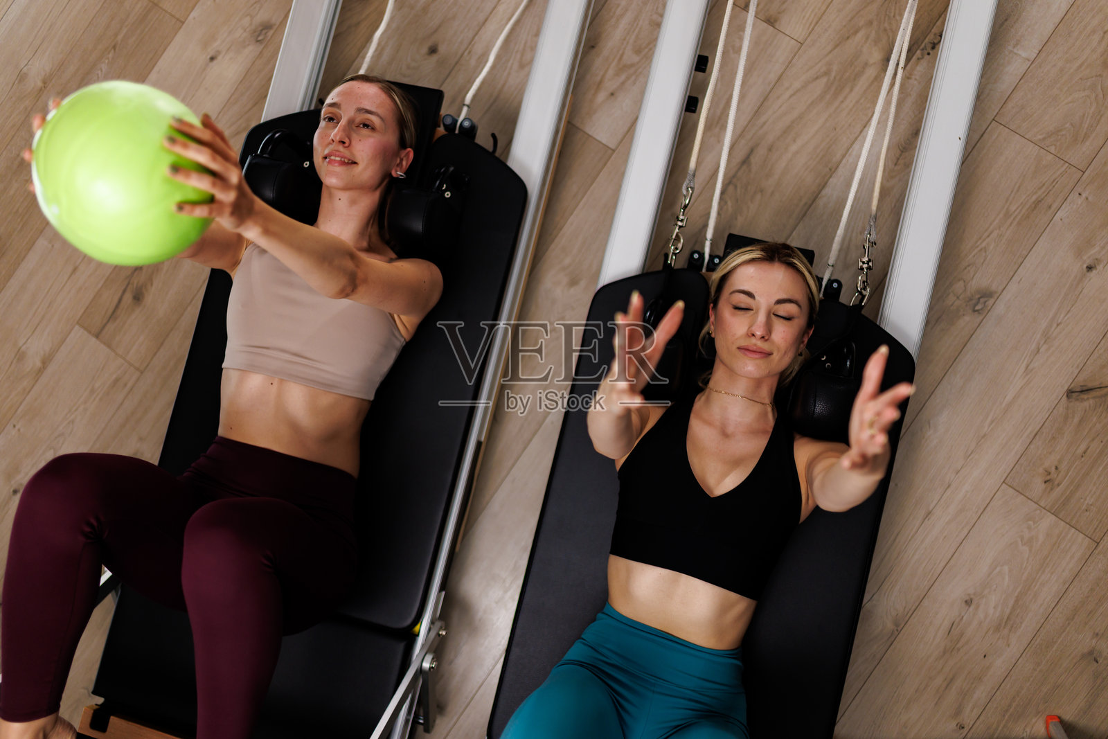 两名女性在明亮的健身房中使用阻力器材进行健身训练,专注于力量和协调的锻炼课程。照片摄影图片