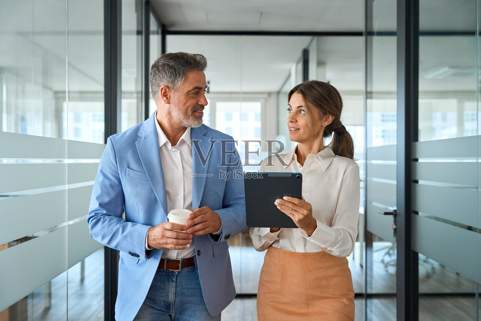 两位忙碌的商务高管在办公室里交谈并走动。照片摄影图片