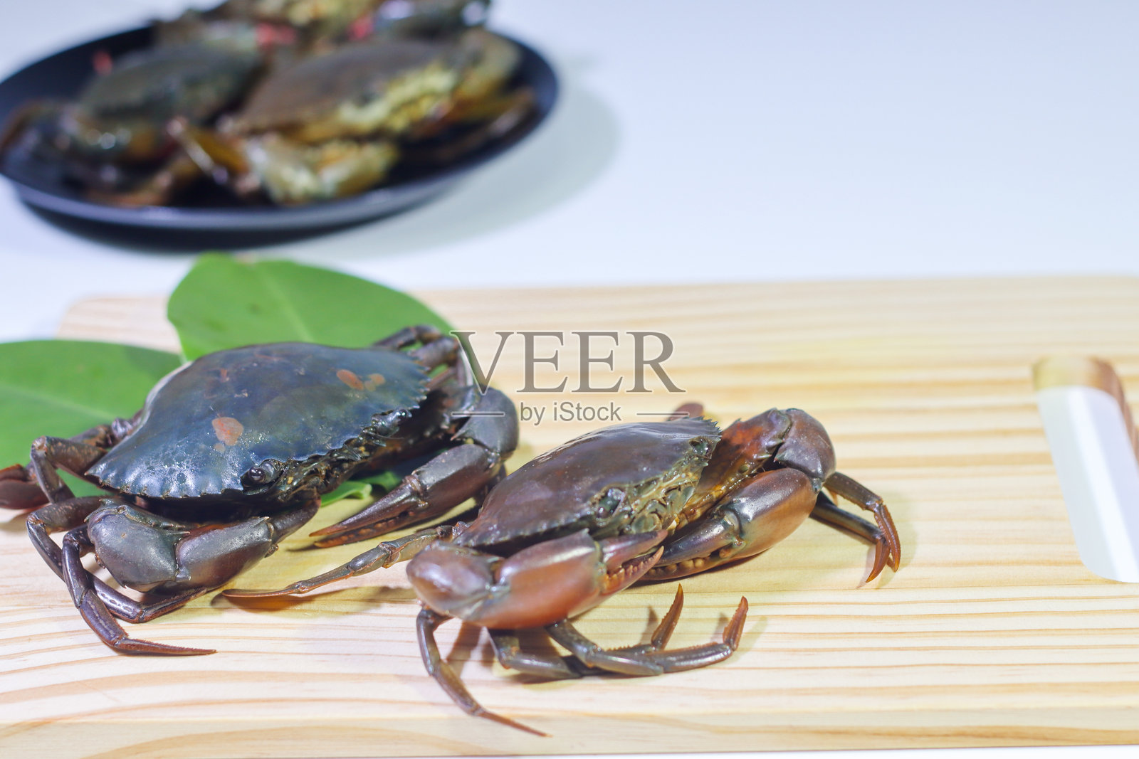 木砧板上的泥蟹,背景中有红树林叶子和黑色盘子里的螃蟹照片摄影图片