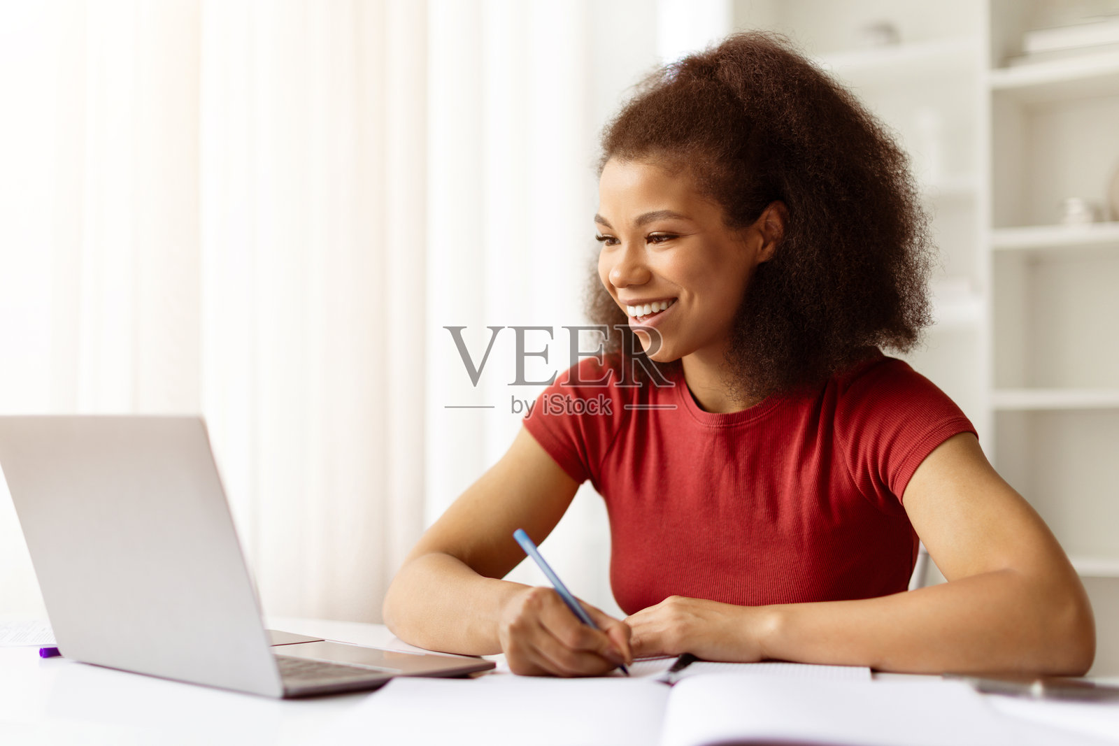 微笑的非裔美国女性在桌子上用笔记本电脑写笔记照片摄影图片