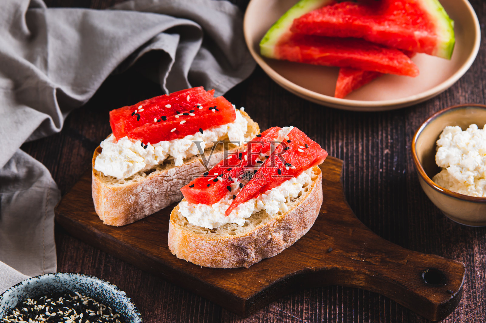 轻盈的烤面包片,上面放有瑞可达奶酪和西瓜,摆放在桌子上的木板上照片摄影图片