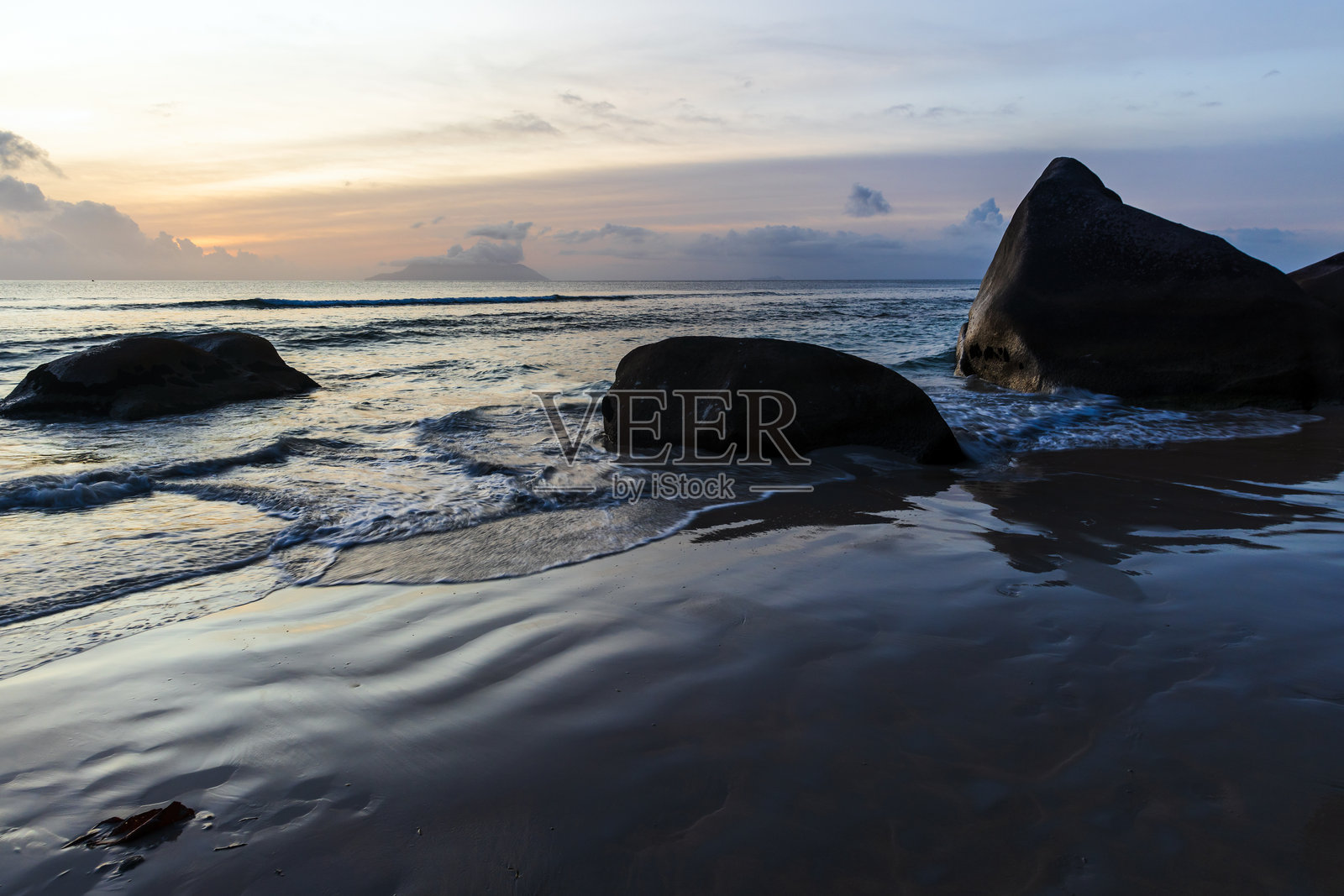 湿沙滩的海滩风景,海岸水域和黑色轮廓的海岸岩石照片摄影图片