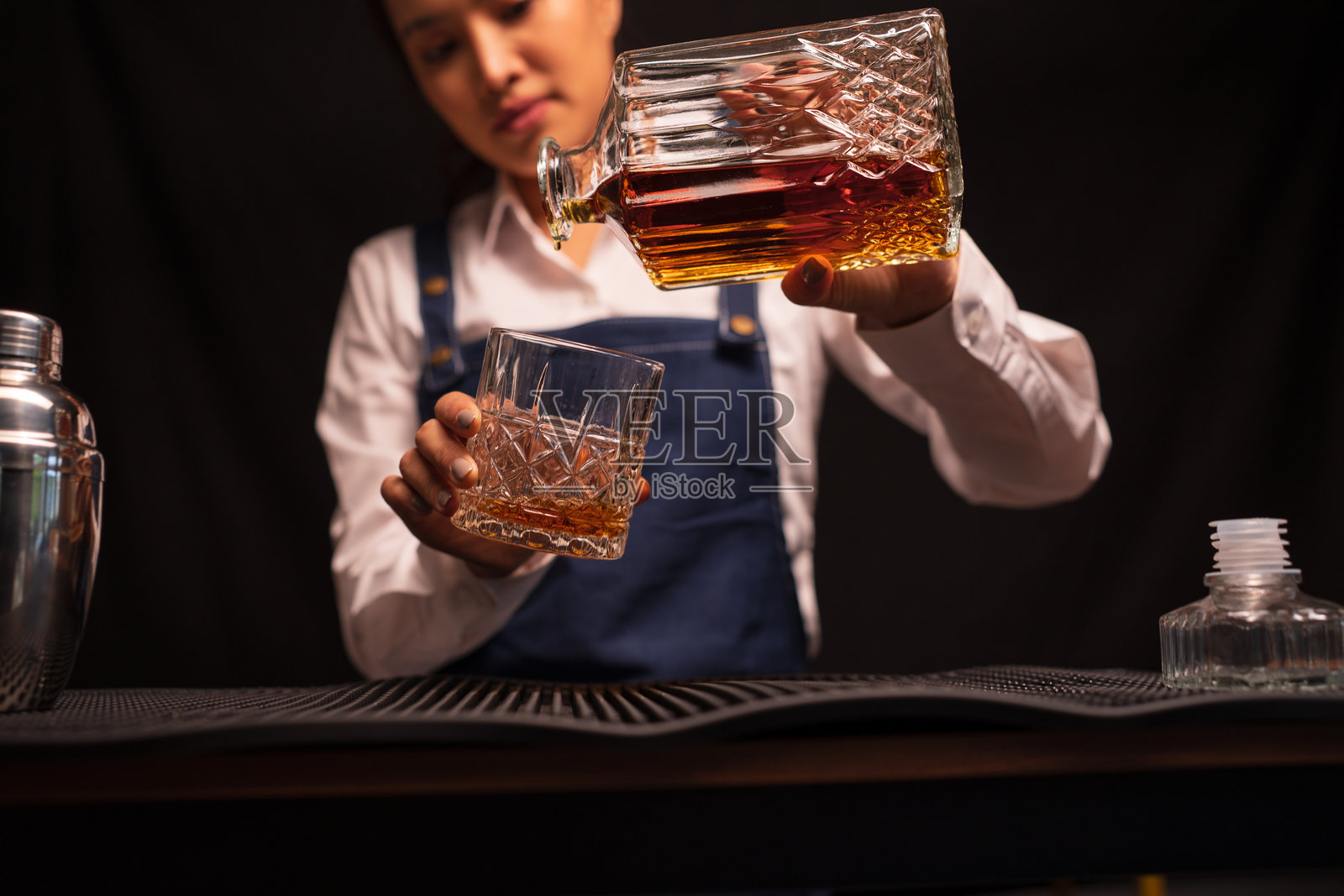 女调酒师在餐厅里将威士忌倒入酒杯。照片摄影图片
