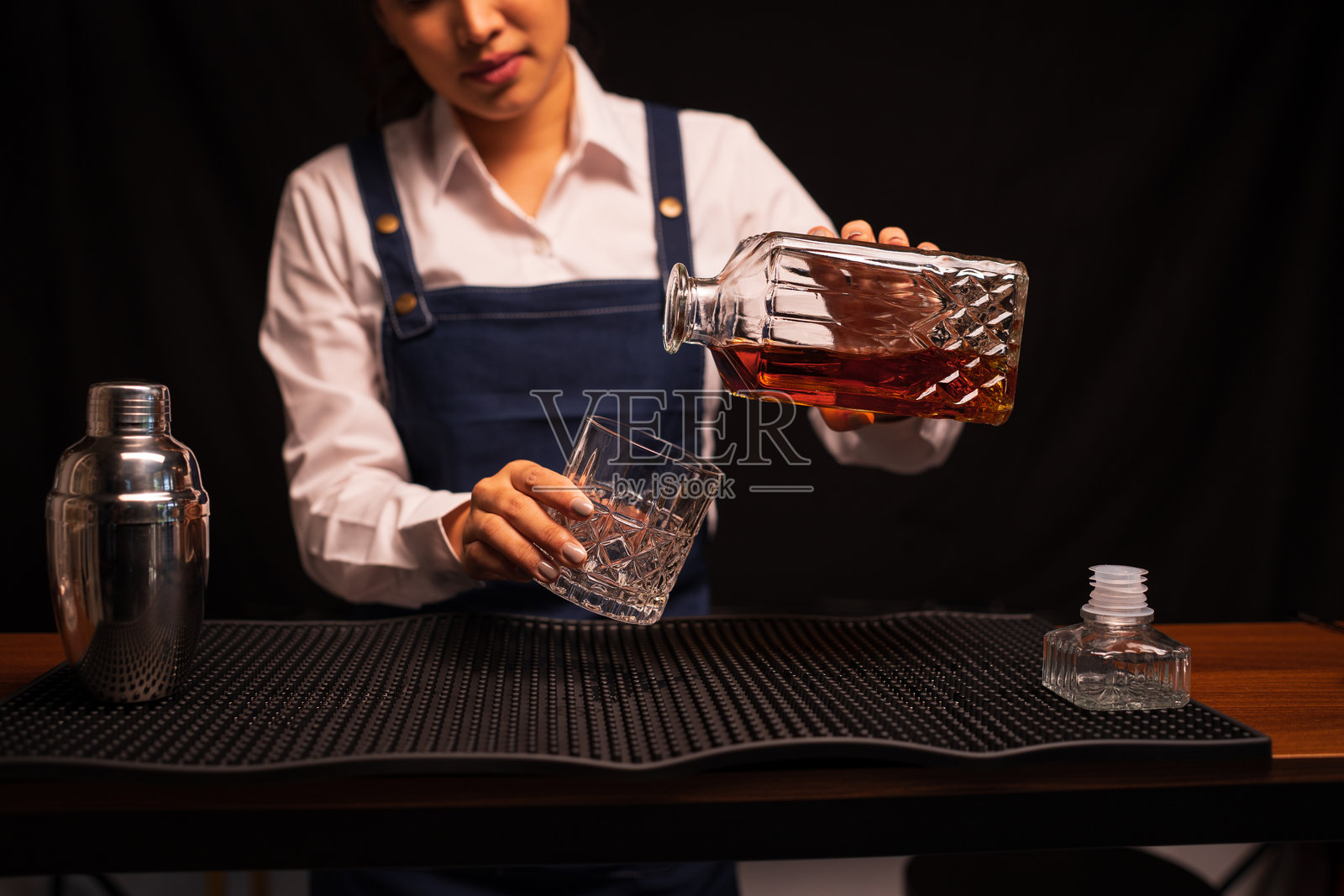 女调酒师在餐厅里将威士忌倒入酒杯。照片摄影图片