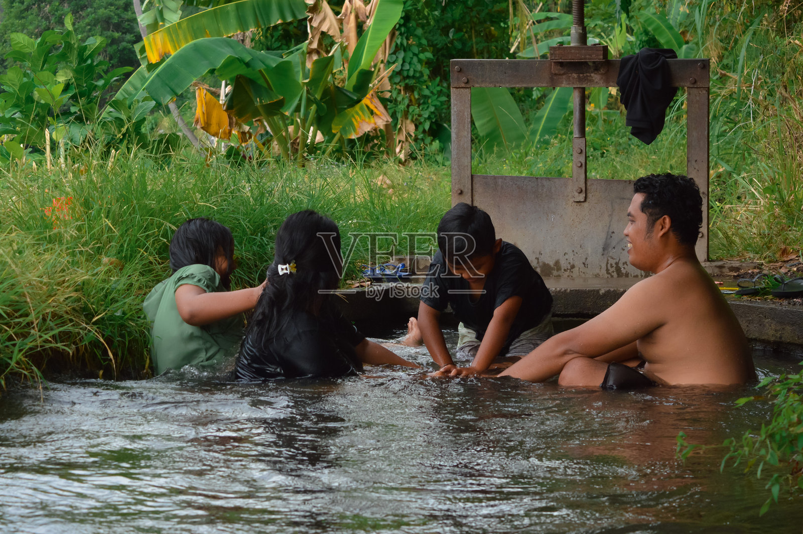 父母手牵手形成屏障,儿子试图穿过溪流。照片摄影图片