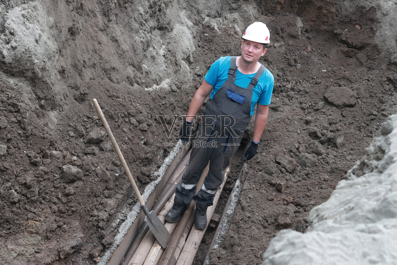 年轻的白人男性建筑工人在挖掘的沟渠中穿着安全装备照片摄影图片