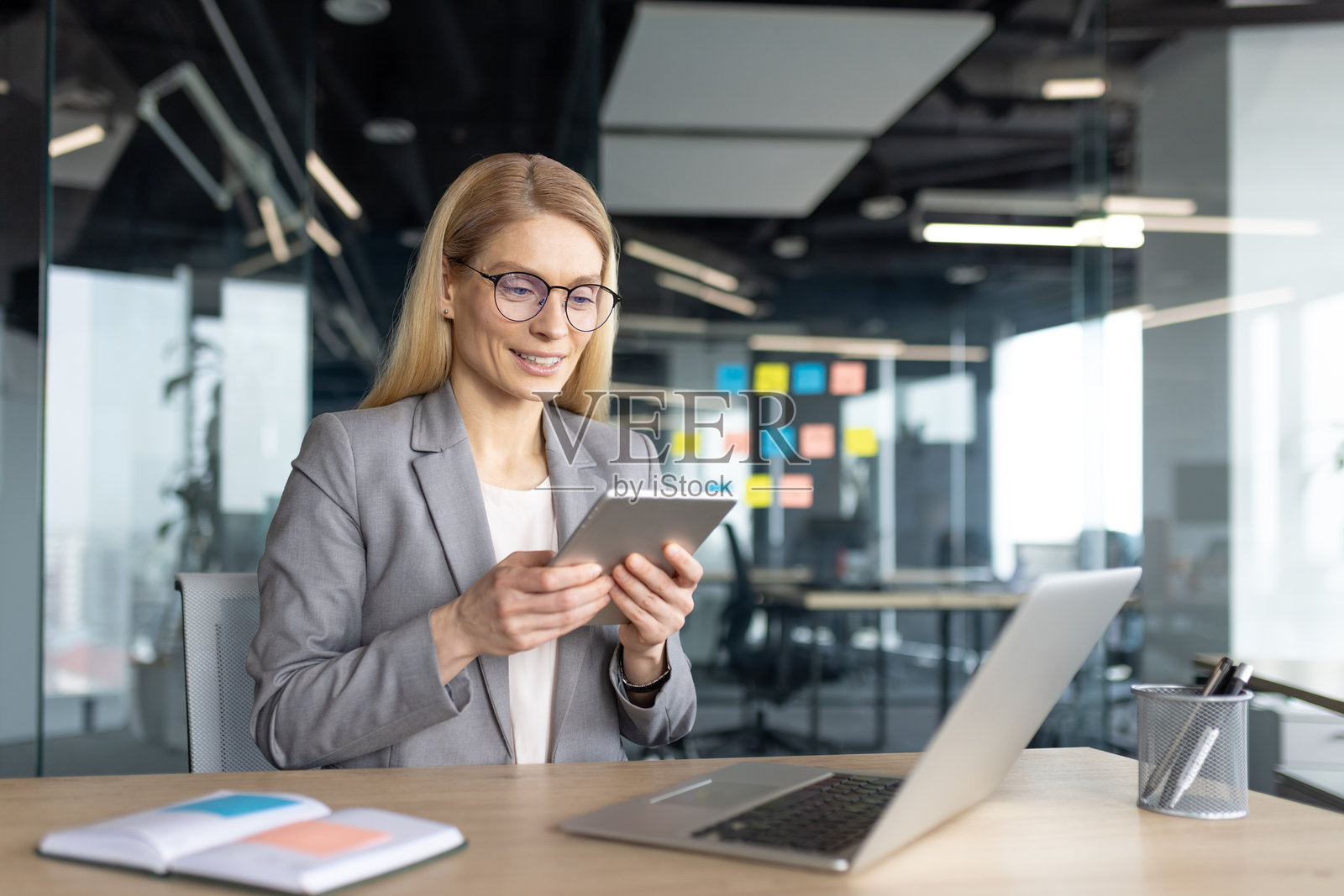 在现代办公室中,一位专注且坚定的女商人在平板电脑上工作。照片摄影图片