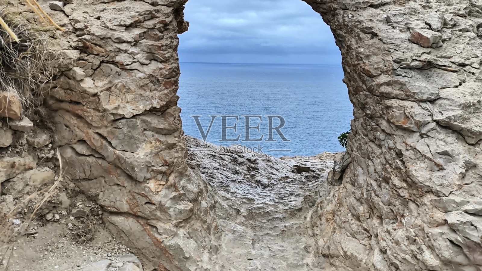 通过崎岖岩石景观中的壮观拱门看到令人叹为观止的海岸风景。照片摄影图片