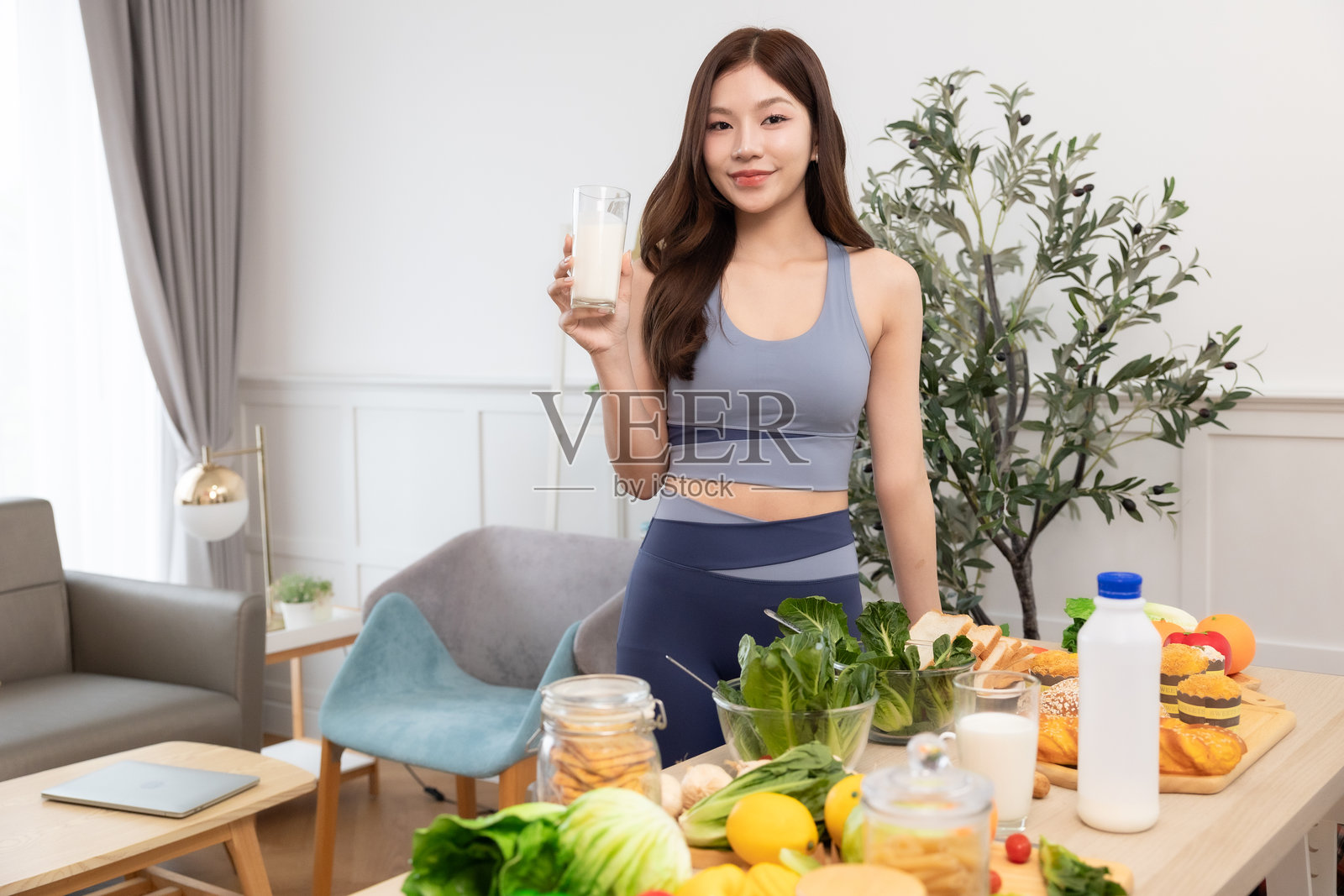 年轻的亚洲运动女性在家准备蛋白质奶昔。饮食与健康食品。训练后放松。美丽的年轻女性在锻炼后喝牛奶。健康生活方式的概念。照片摄影图片