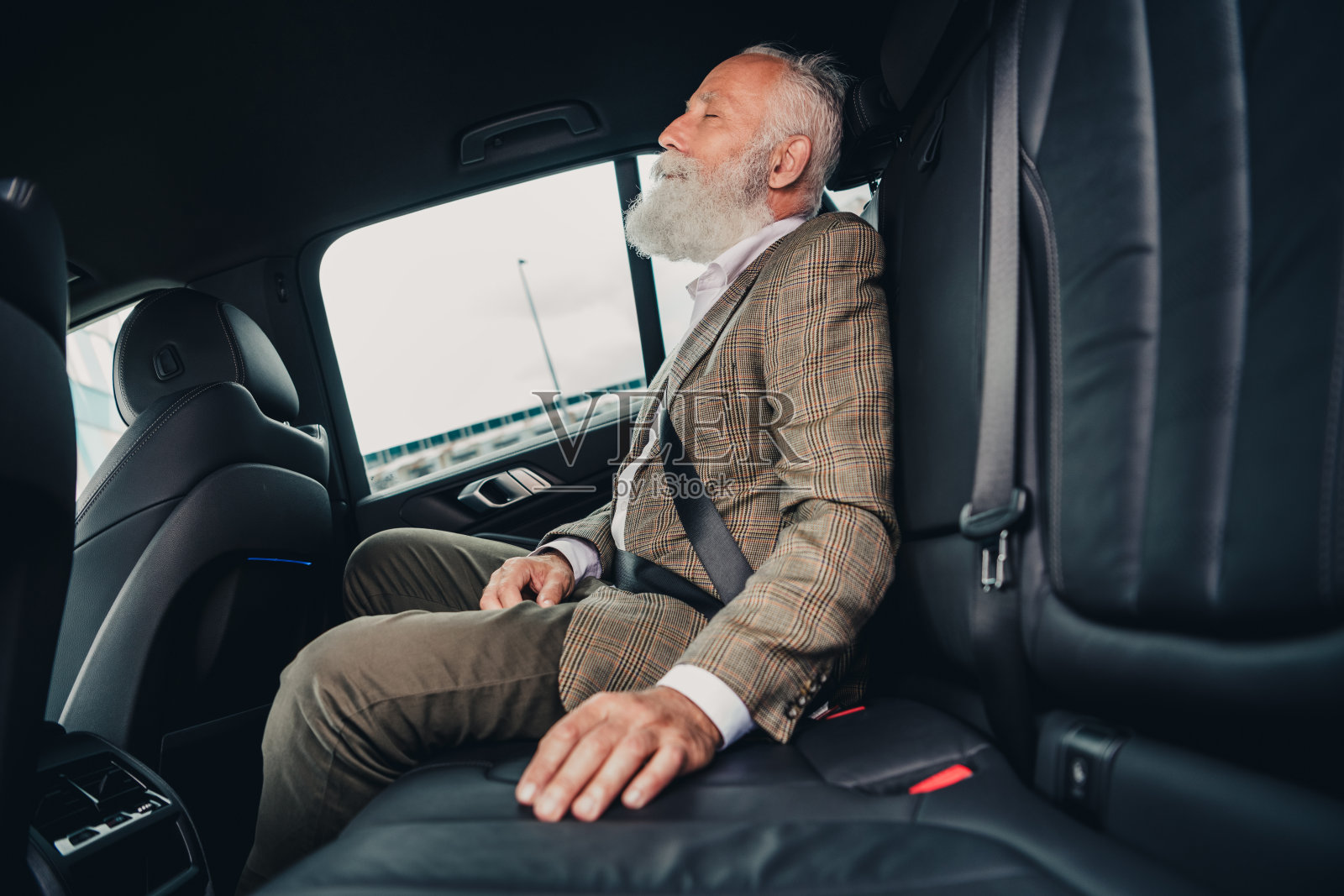 身穿西装的英俊绅士坐在汽车座椅上,展现出在城市旅行中的自信与优雅。照片摄影图片