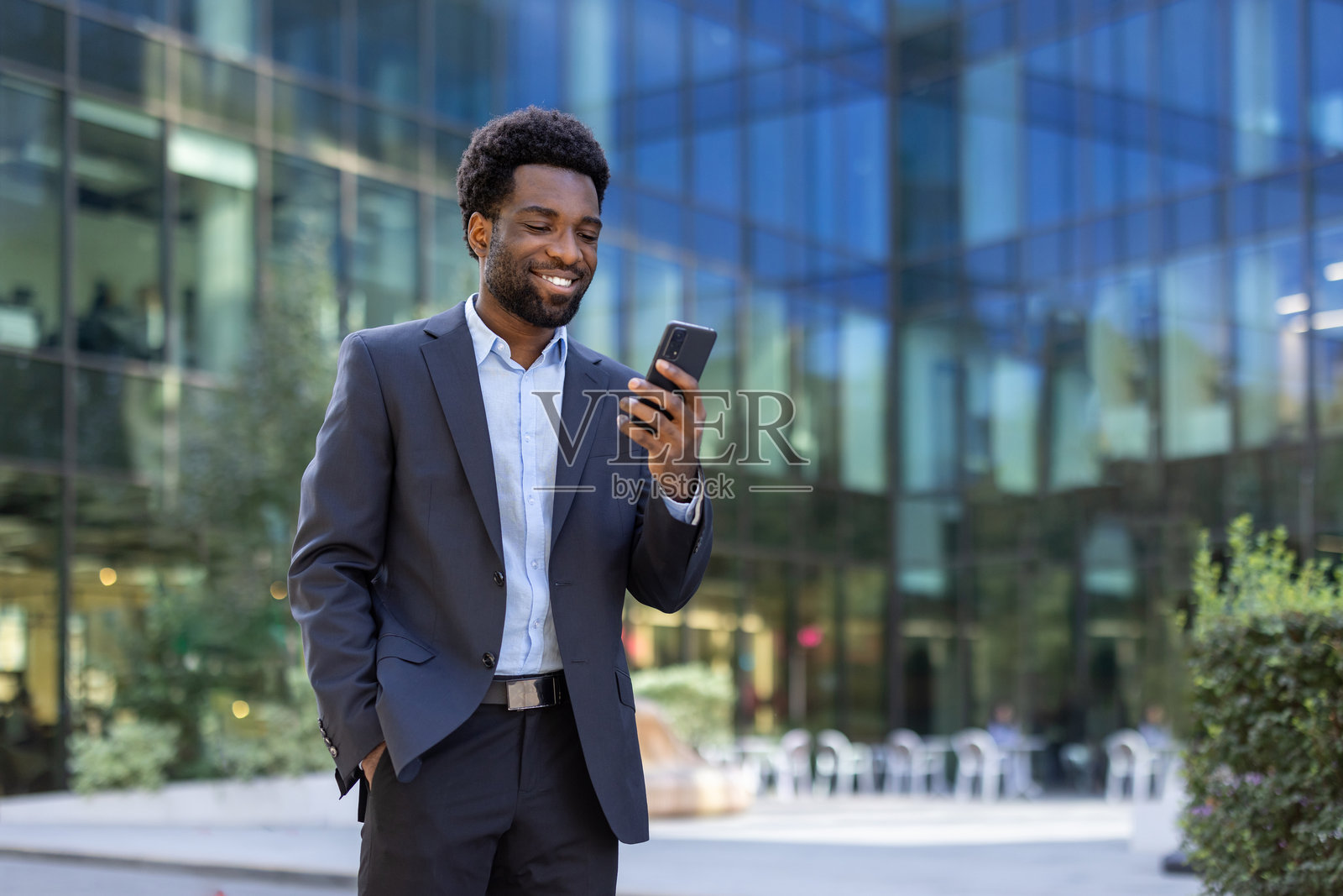 一位微笑的商人在现代办公大楼外查看手机。照片摄影图片