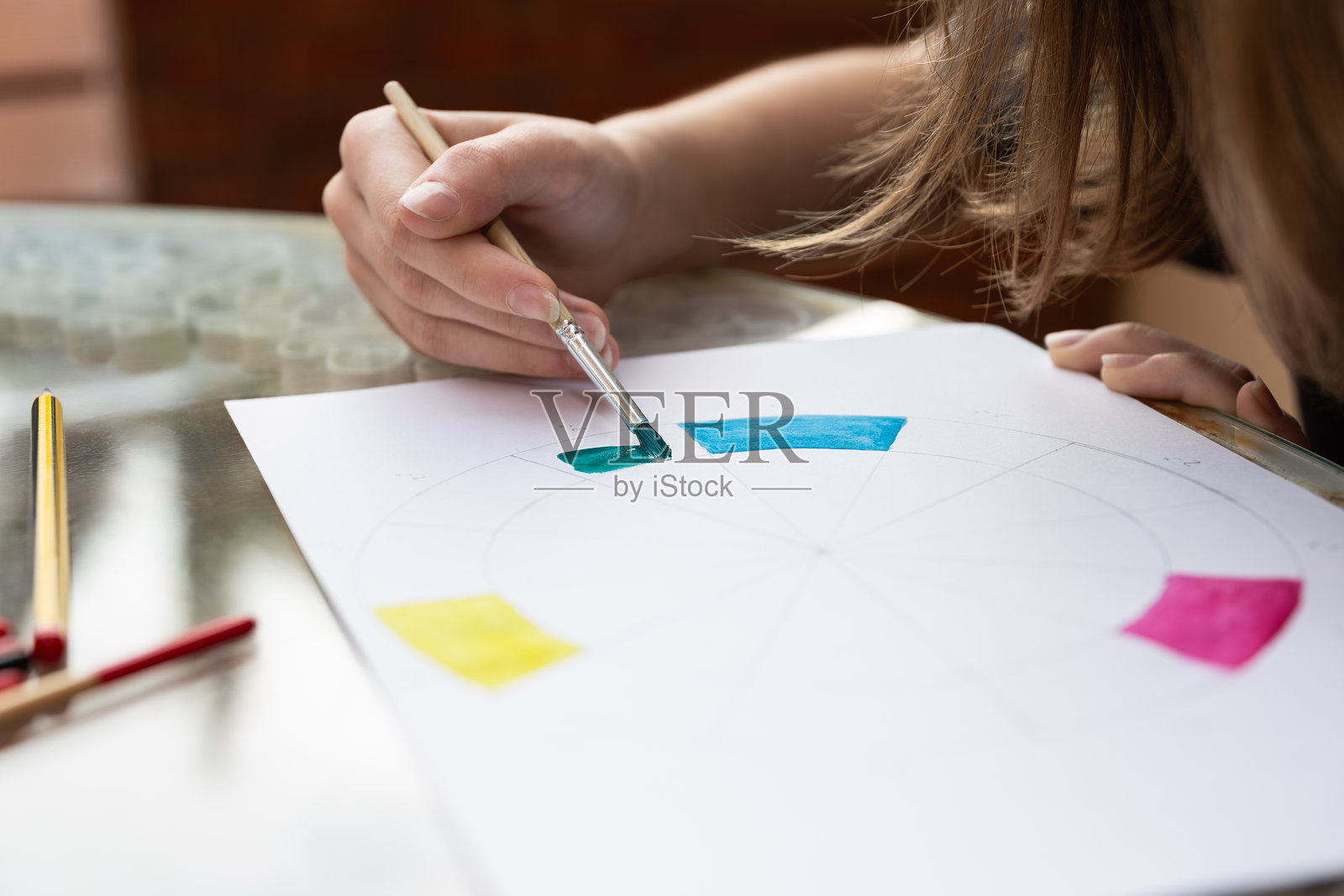 女性手在色轮图上涂抹蓝色水彩,周围有铅笔和画笔。户外环境,自然光照。留白空间。教育艺术和创造性专注的概念。照片摄影图片