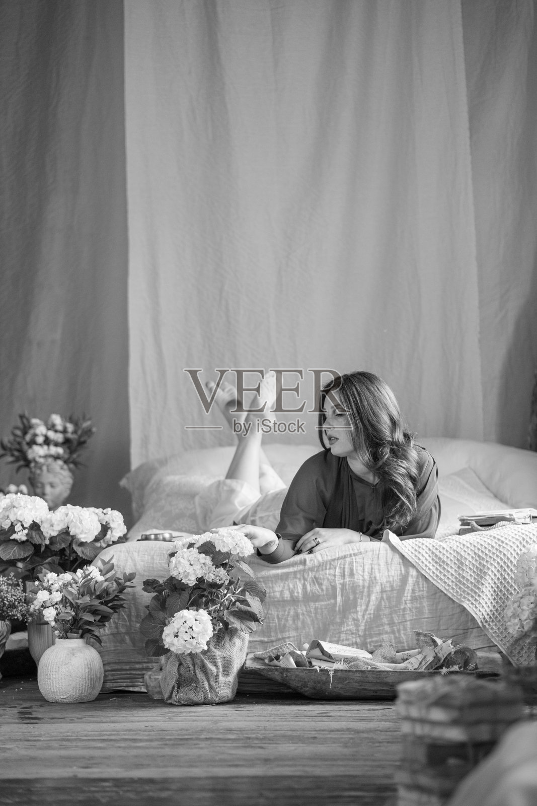 美丽的年轻女性在复古风格的房间里床上摆姿势,周围有很多花。背景是工业风格的砖墙。照片摄影图片