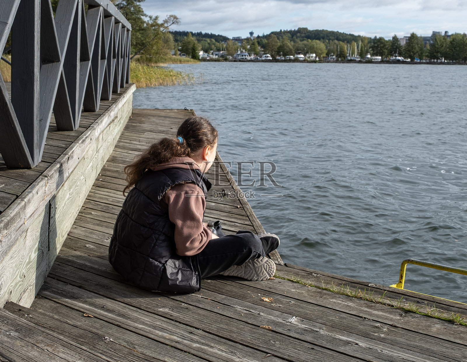 一个10岁的白人女孩坐在湖边的木栈道上,喝着汽水。她在湖边放松。照片摄影图片