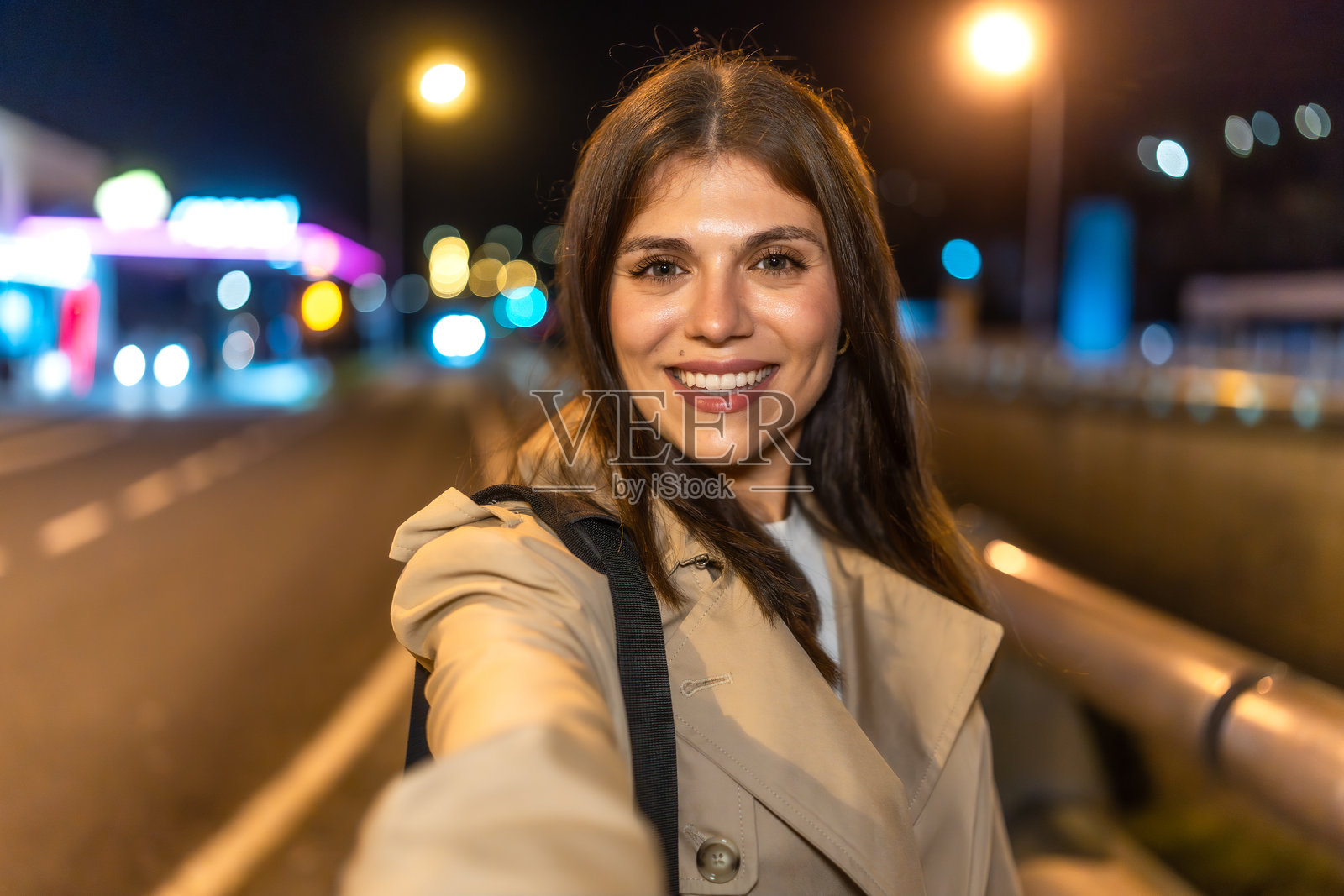 年轻女性在城市街道上微笑着自拍,夜晚的氛围。照片摄影图片