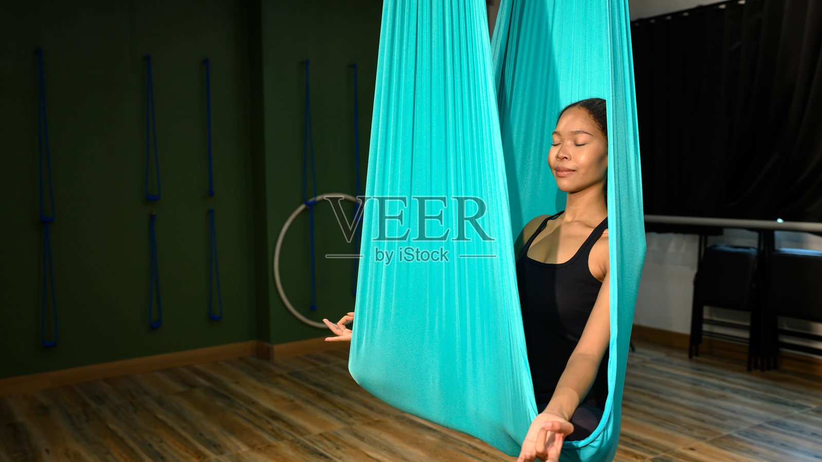 年轻女子在宁静的教室里,在空中瑜伽吊床中冥想。照片摄影图片