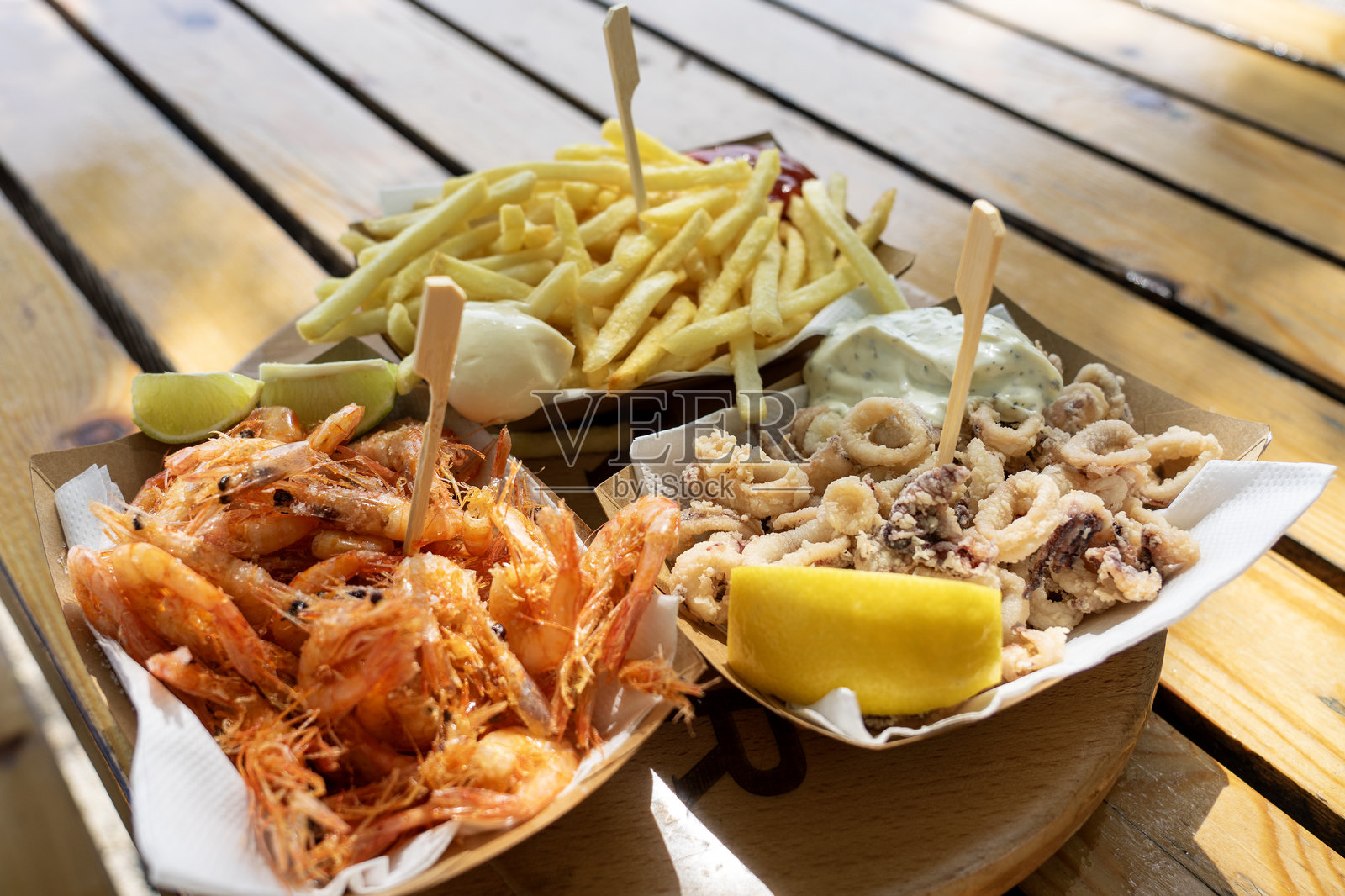 炸虾、炸鱿鱼圈和薯条配酱料和柠檬在户外供应照片摄影图片