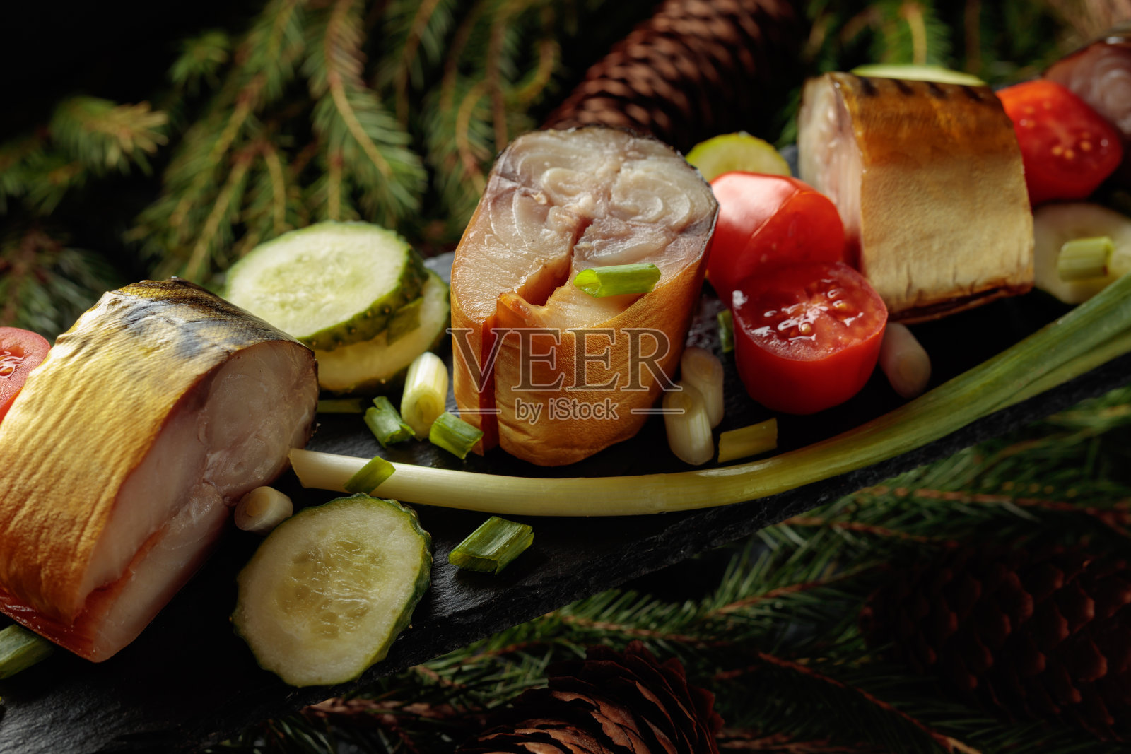 烟熏鲭鱼配新鲜黄瓜、番茄和葱,放在黑盘子上。照片摄影图片