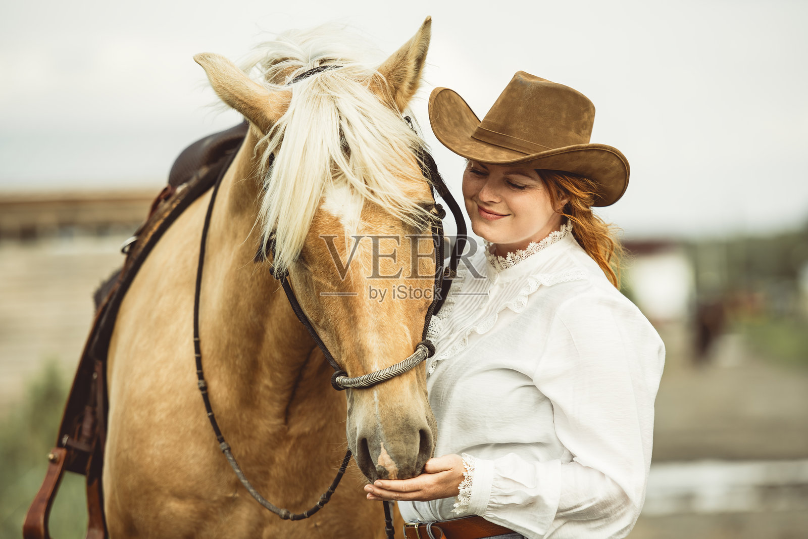 一位女士自豪地戴着牛仔帽,站在她的马旁边照片摄影图片