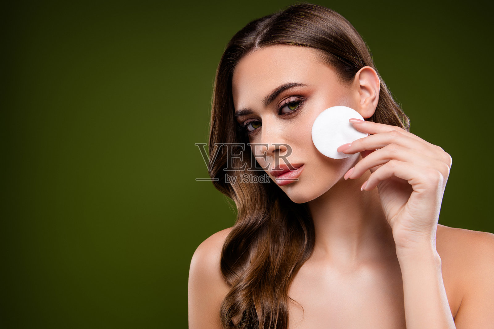 一位迷人的女性肖像,在深绿色背景下用化妆棉展示健康的肌肤护理照片摄影图片