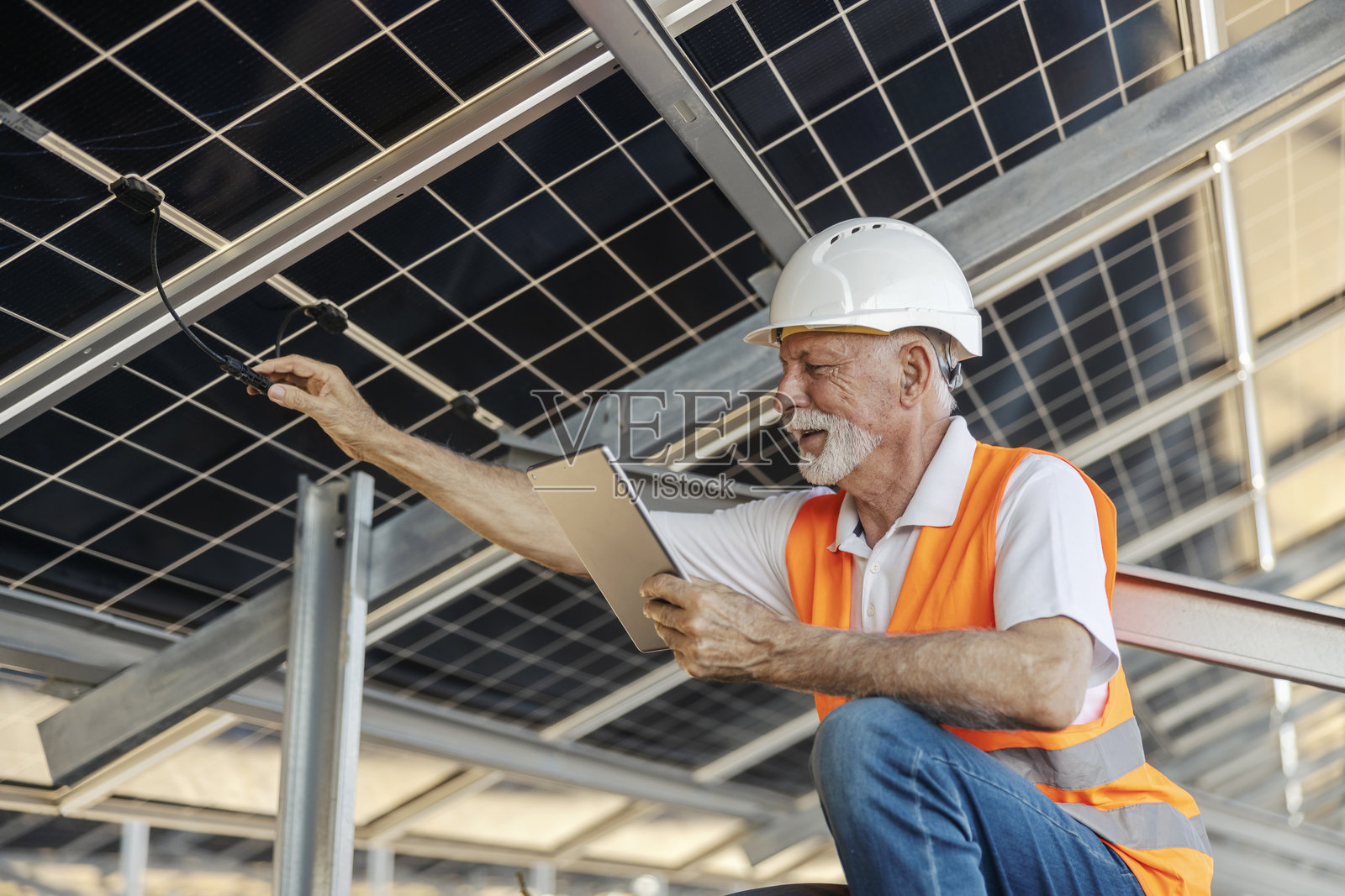 身着安全装备的年长男性工人正在使用平板电脑检查太阳能电池板照片摄影图片