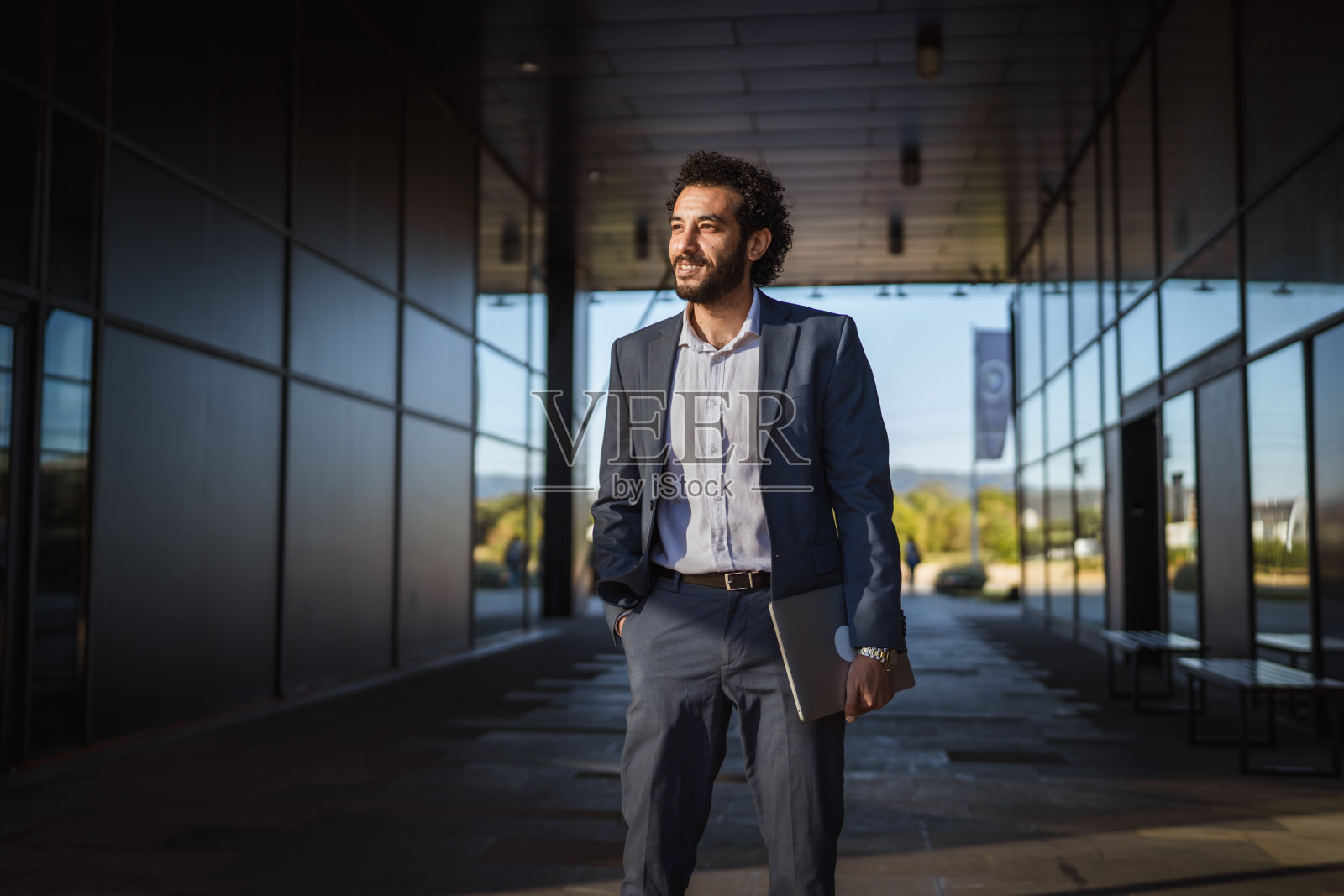 自信的商人拿着笔记本电脑走出办公楼照片摄影图片