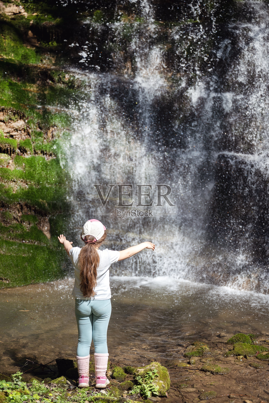 一个孩子站在山间的瀑布前照片摄影图片