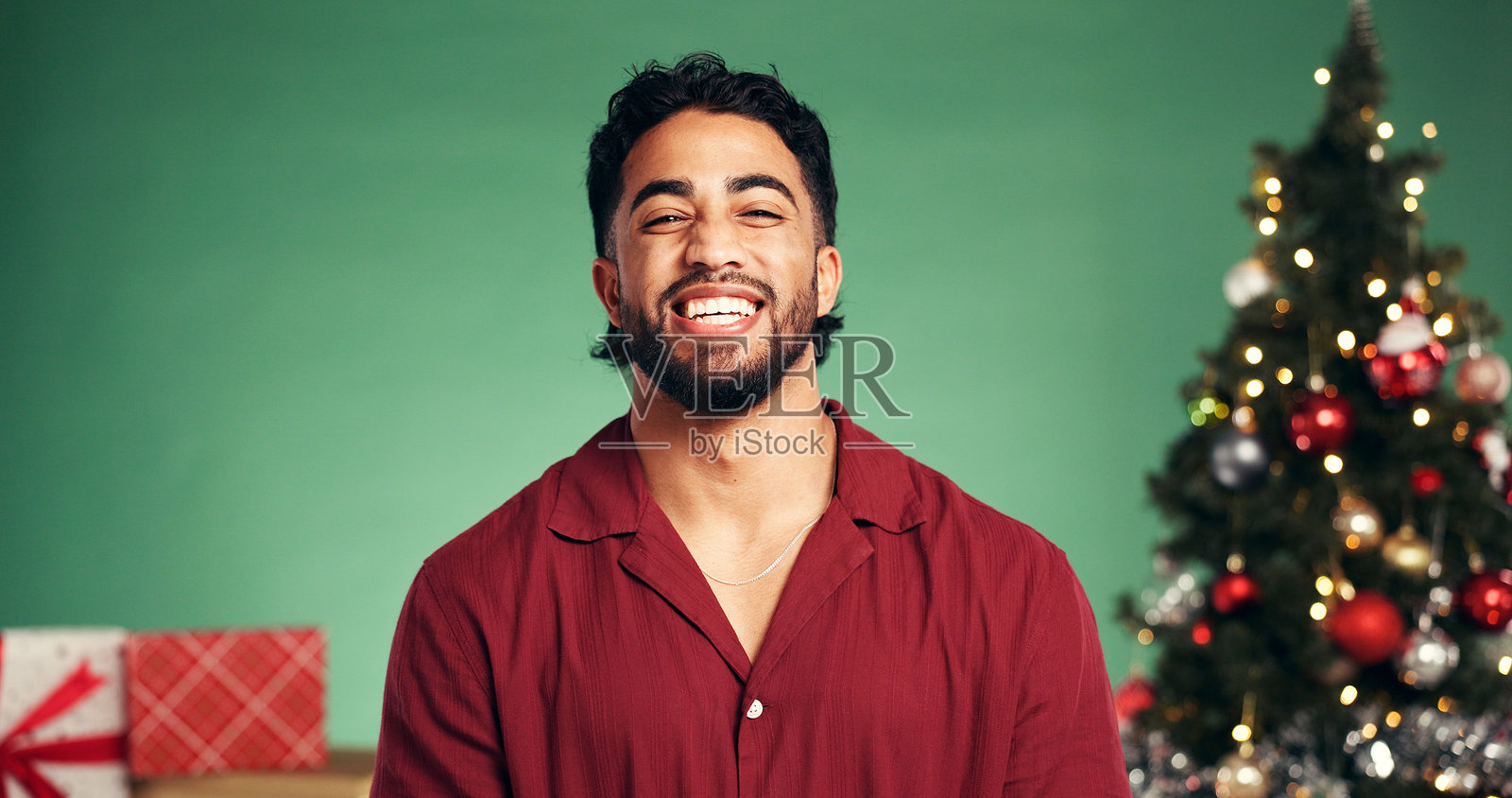 工作室里,一名男子正在圣诞装饰或礼物前开怀大笑,庆祝节日。背景为绿色,营造出圣诞季、十二月或挂满装饰物的圣诞树的节日氛围,展现出幸福和喜悦。照片摄影图片
