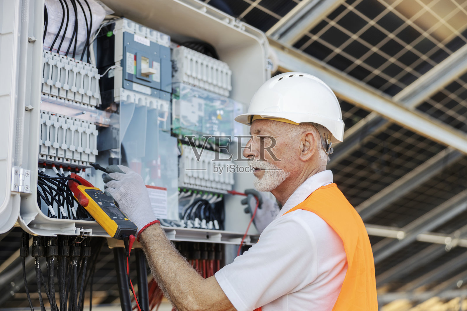 老年男性工人在太阳能产业现场检查太阳能电池板的电气元件进行维护照片摄影图片