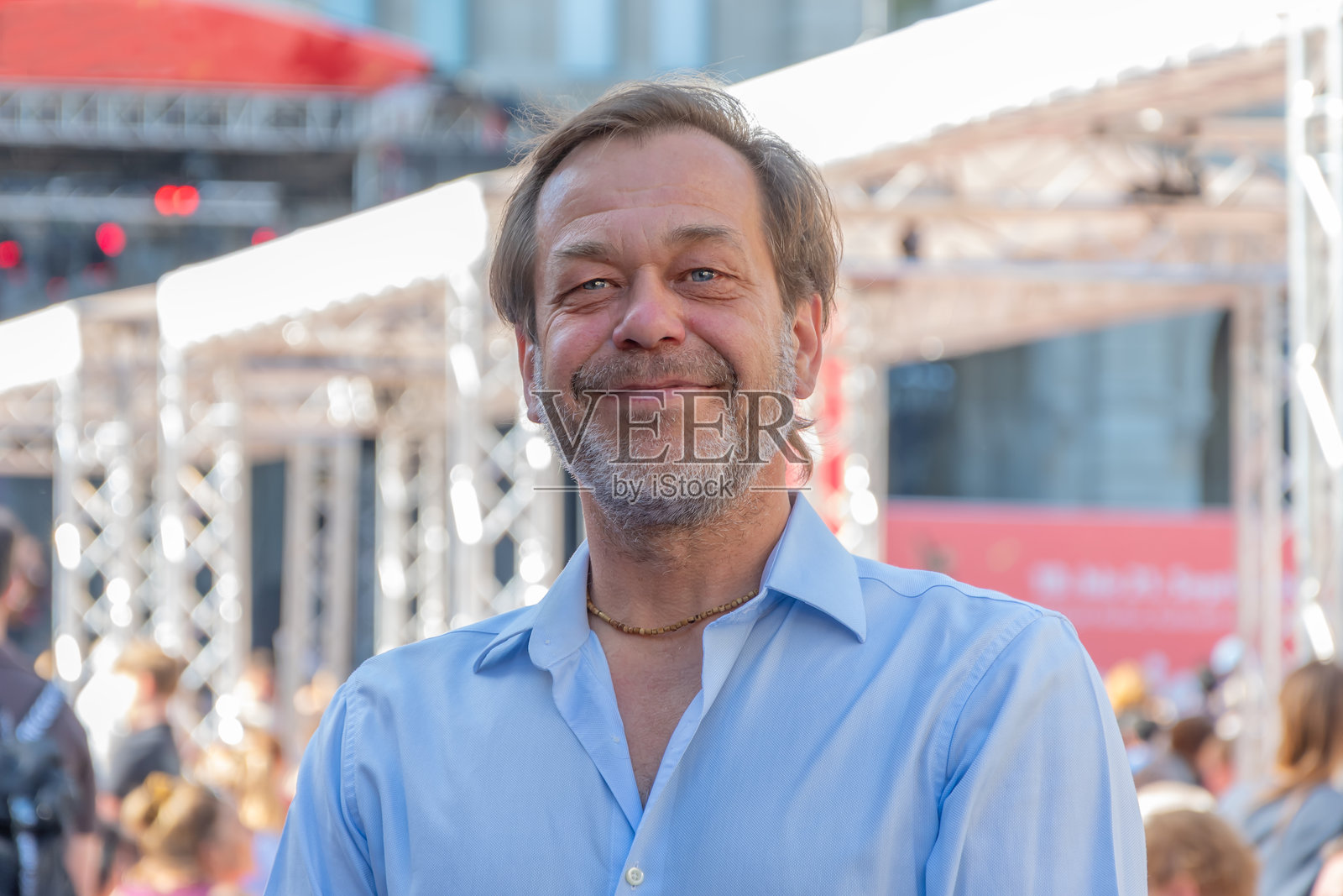一位留着胡须、穿着衬衫的老年男子站在街上,周围是人群和建筑。照片摄影图片