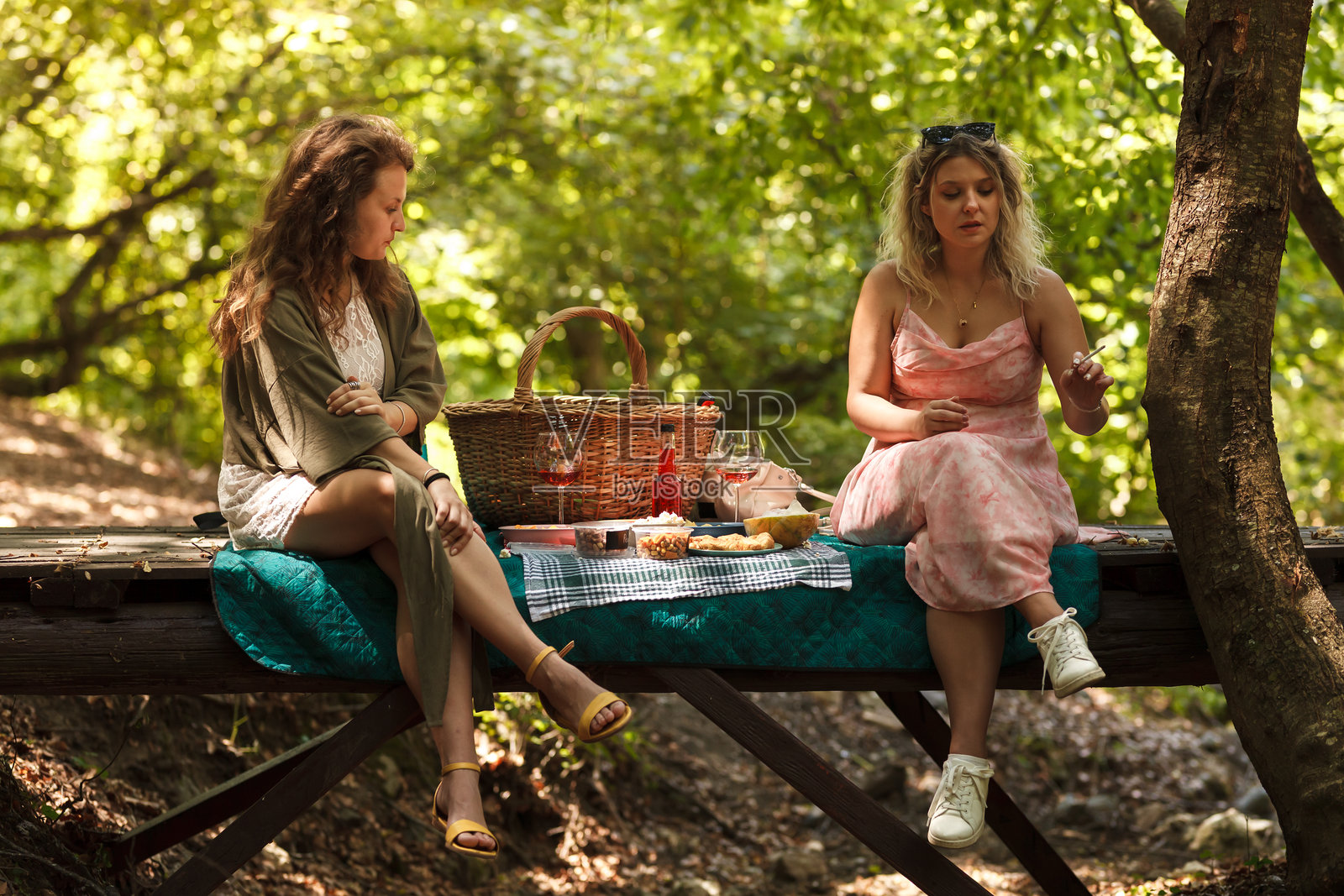 阳光明媚的午后,两位朋友在郁郁葱葱的绿意环绕的木制平台上享受野餐,置身于宁静的自然环境中。照片摄影图片