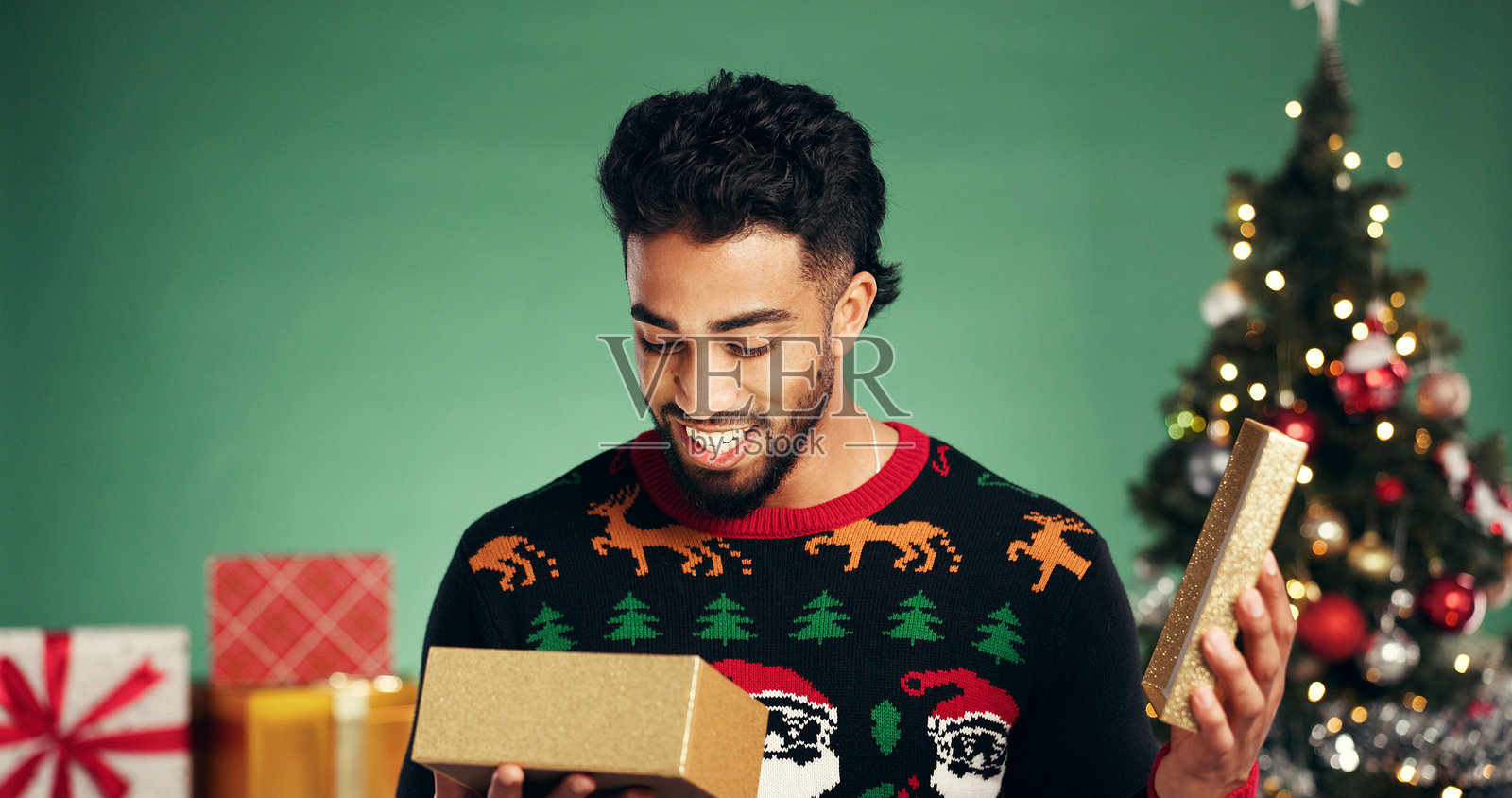 男人,圣诞节在影棚,为礼物感到高兴,有盒子和节日庆典,背景是绿色的节日季。有圣诞树、散景和面带微笑的男性,为礼物、传统或圣诞包装。照片摄影图片