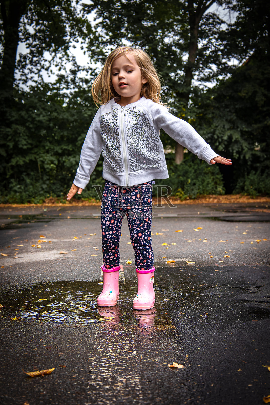 穿着粉色雨靴的小女孩在户外水坑里玩耍照片摄影图片