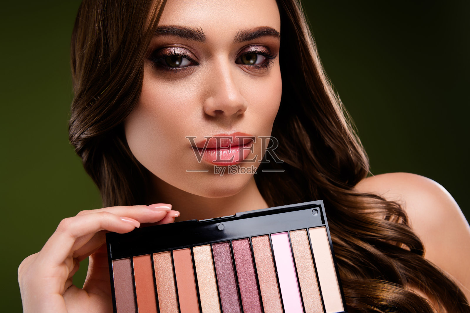 特写镜头,一位美丽的年轻女子在绿色背景前展示着带有色彩的化妆调色盘。照片摄影图片