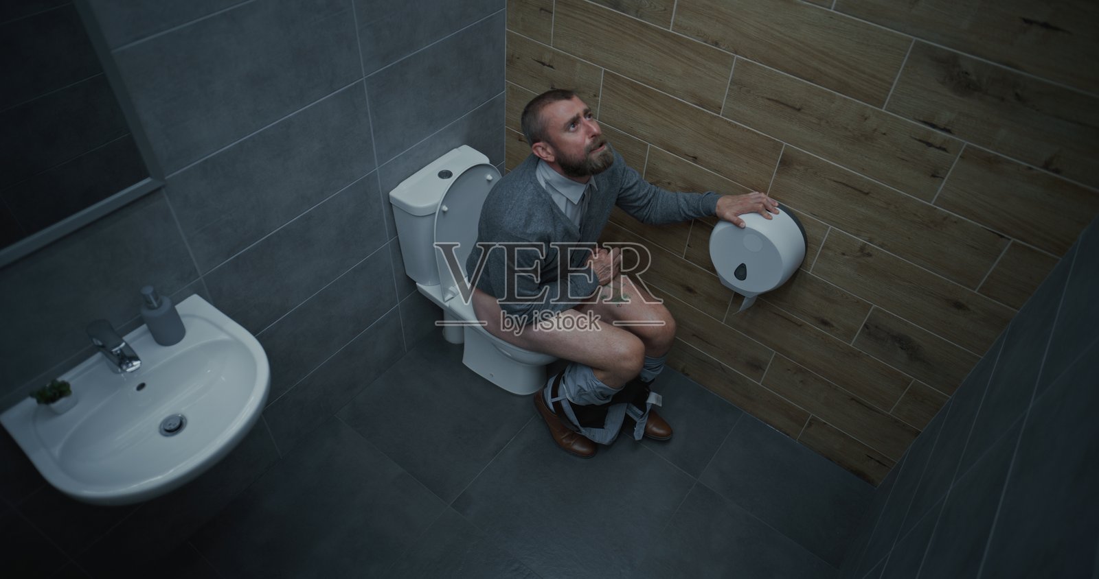 商人坐在马桶上脱裤子,患有腹泻和消化不良。照片摄影图片