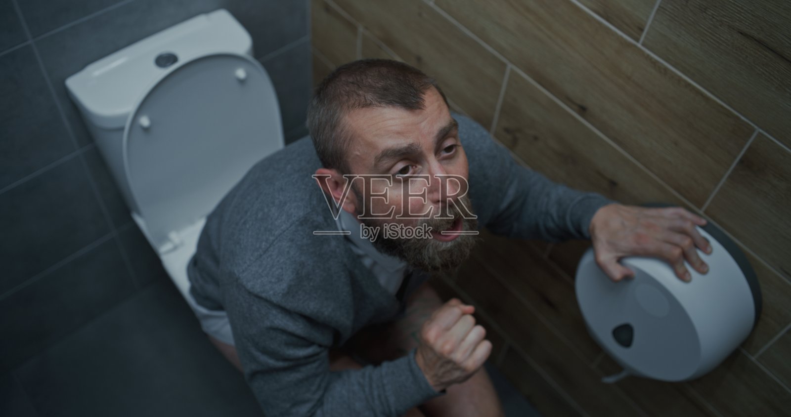 腹泻和消化不良的商人,面部表情紧张,坐在马桶上照片摄影图片