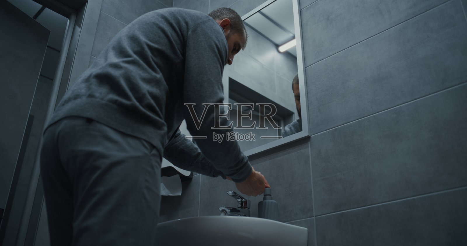 商务男士在现代办公室的洗手间用肥皂洗手,并照着镜子。照片摄影图片